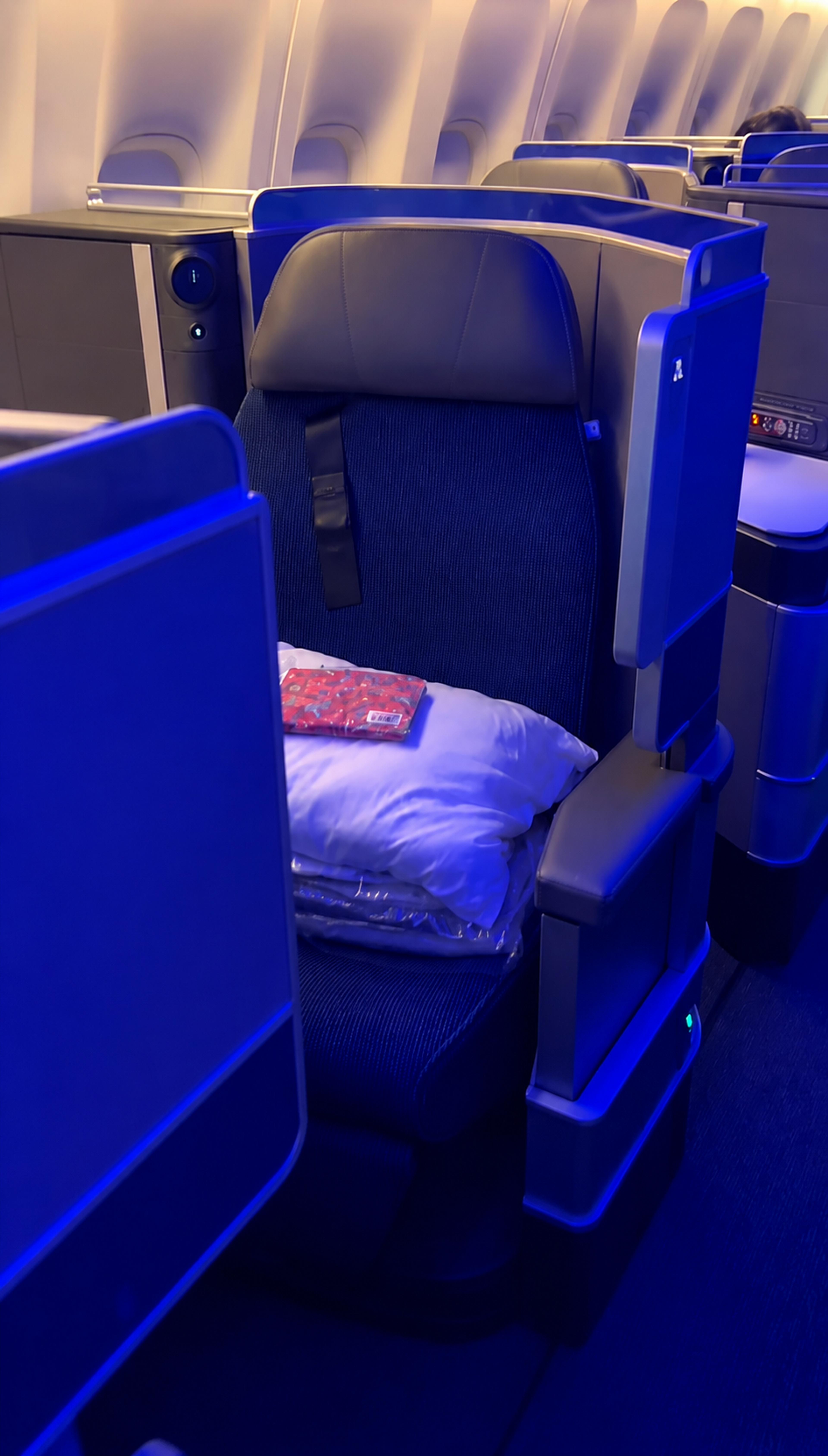 A luxurious first class seat inside a commercial airplane cabin, illuminated with ambient blue lighting.