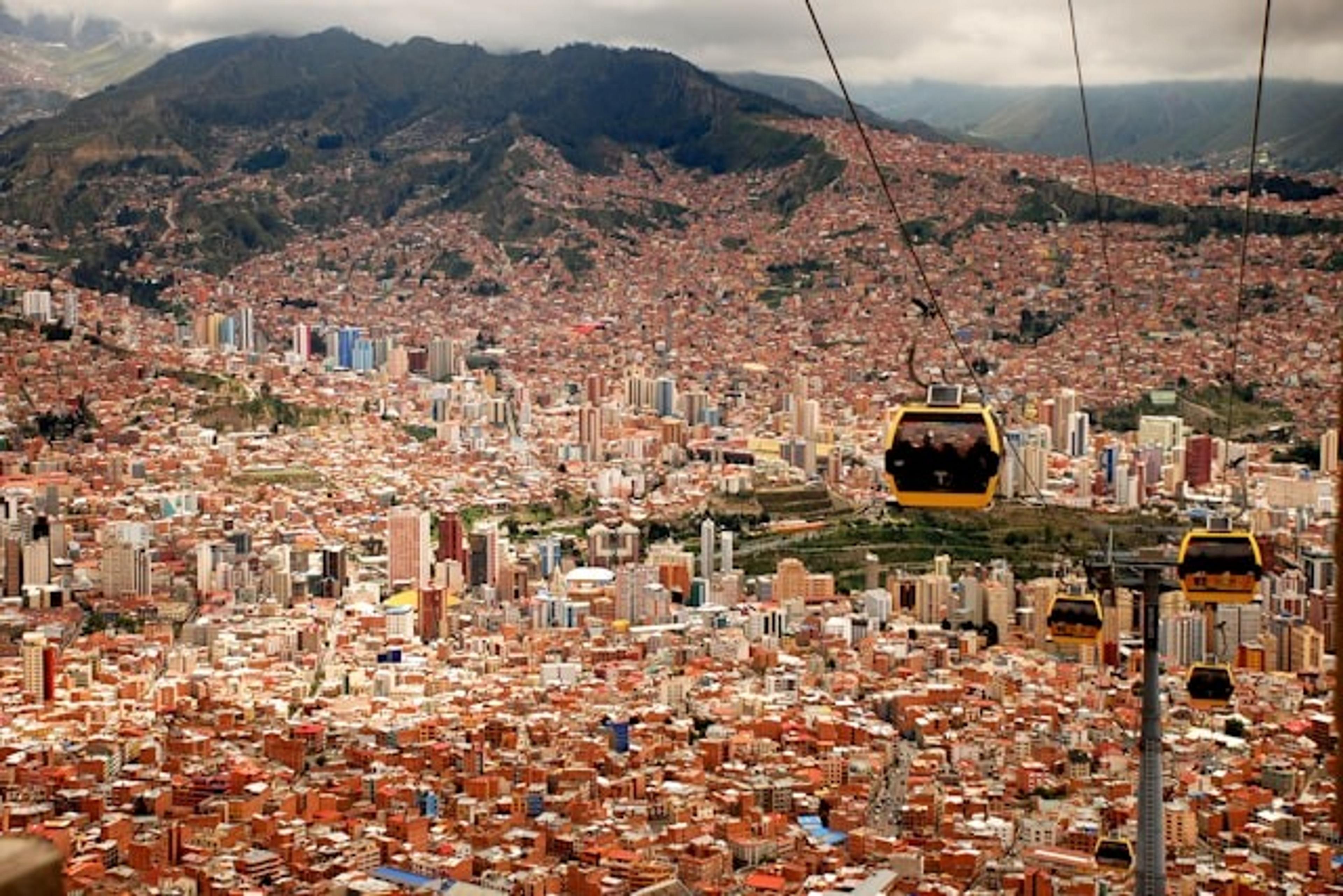 La Paz, Bolivia sprawls below with cable cars traversing above the vibrant cityscape and mountains in the distance.