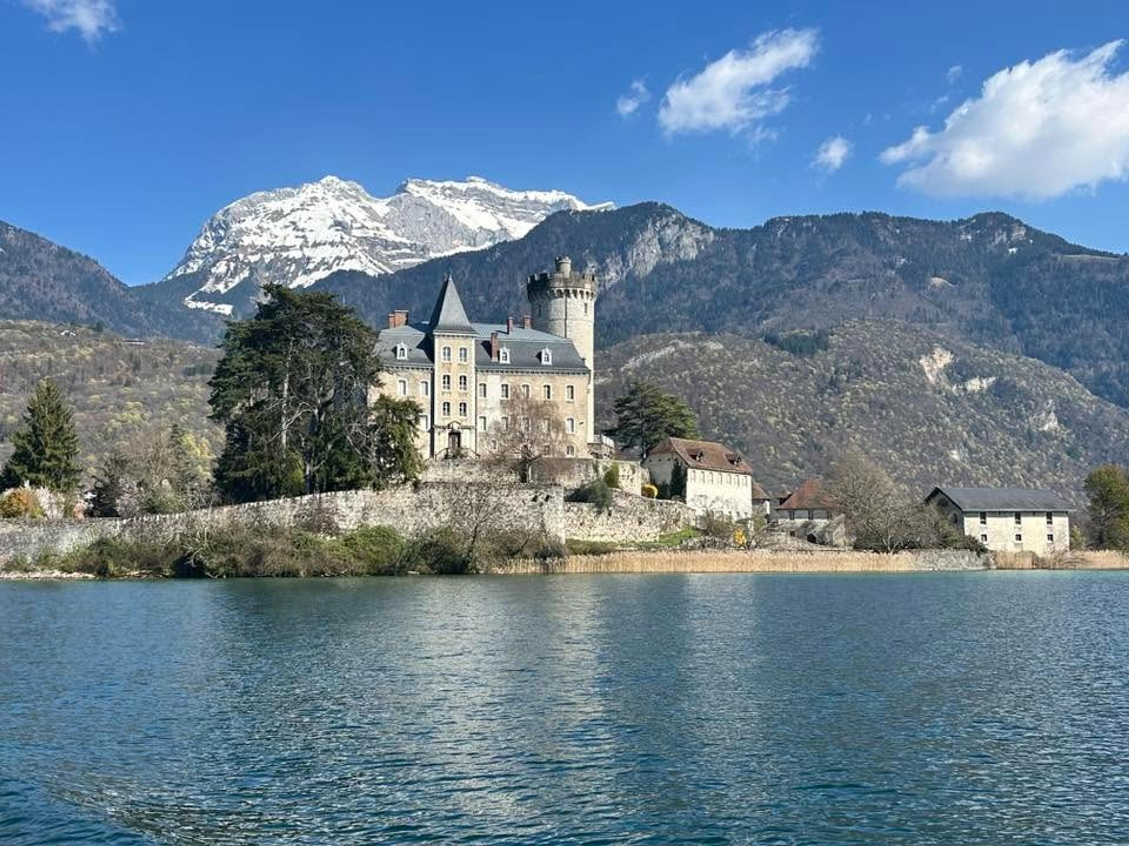 Château de Duingt sits on the scenic edge of Lake Annecy in France, framed by snow-capped mountains.