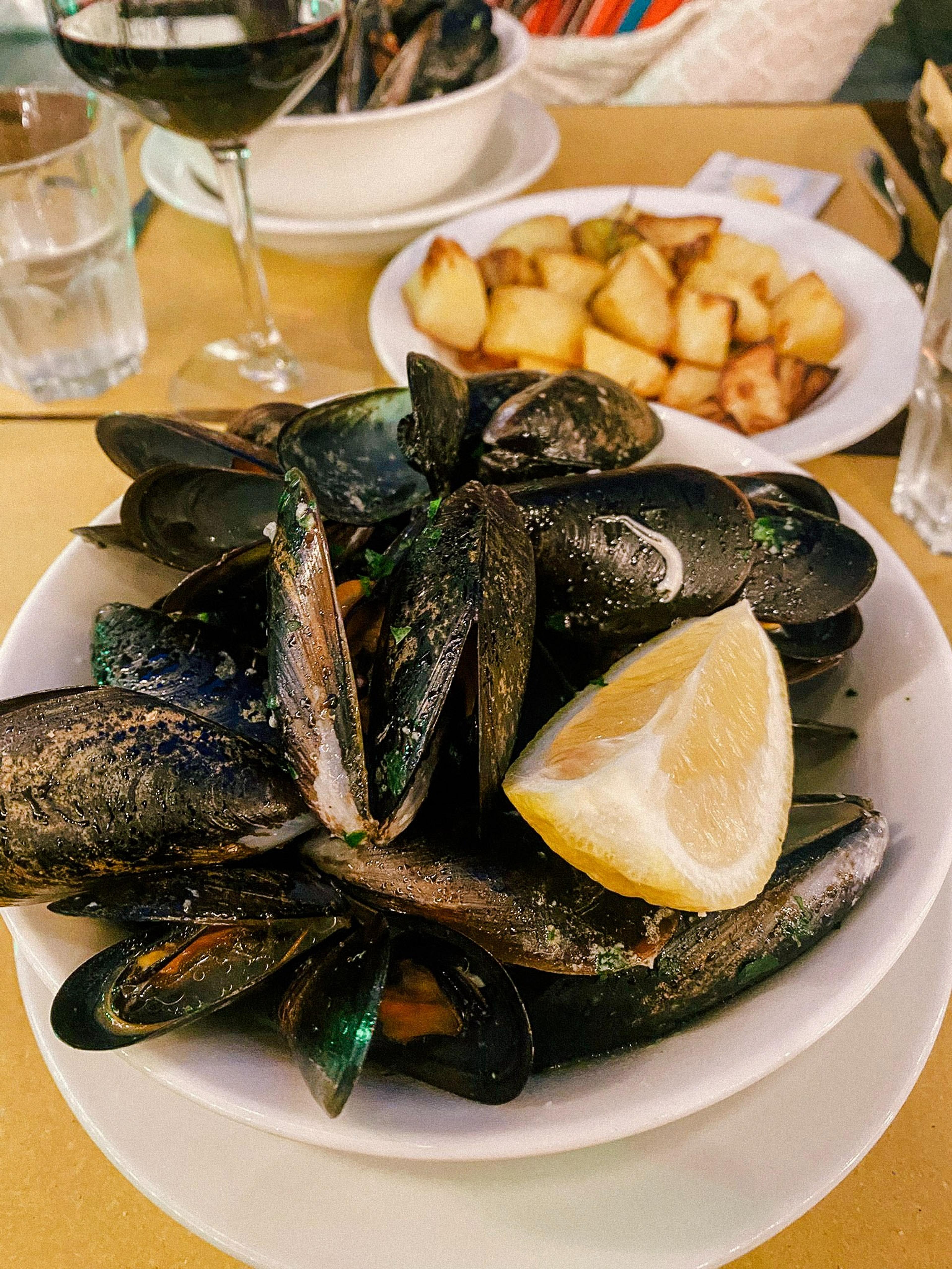 A plate of mussels with lemon is served at a cozy restaurant in Sestri Levante
 with glasses of wine and roasted potatoes.