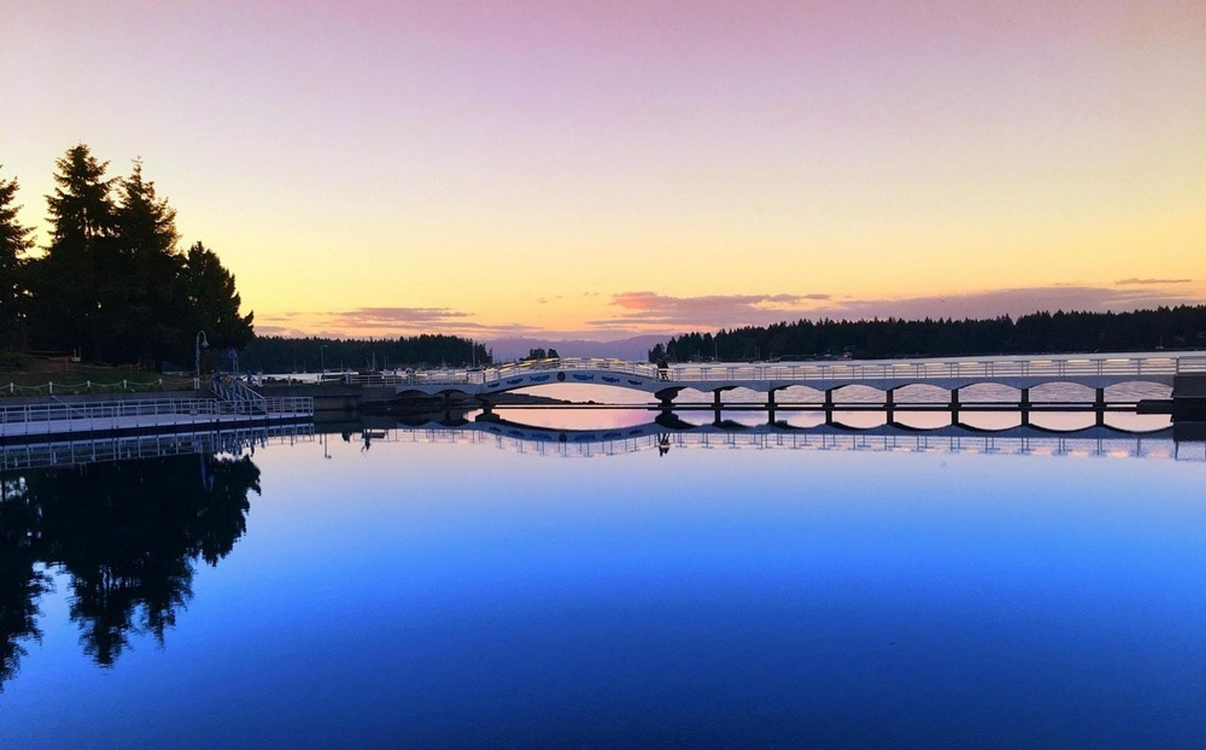 A serene sunset casts a colorful reflection over the iconic wooden bridges spanning the calm waters of Nanaimo.