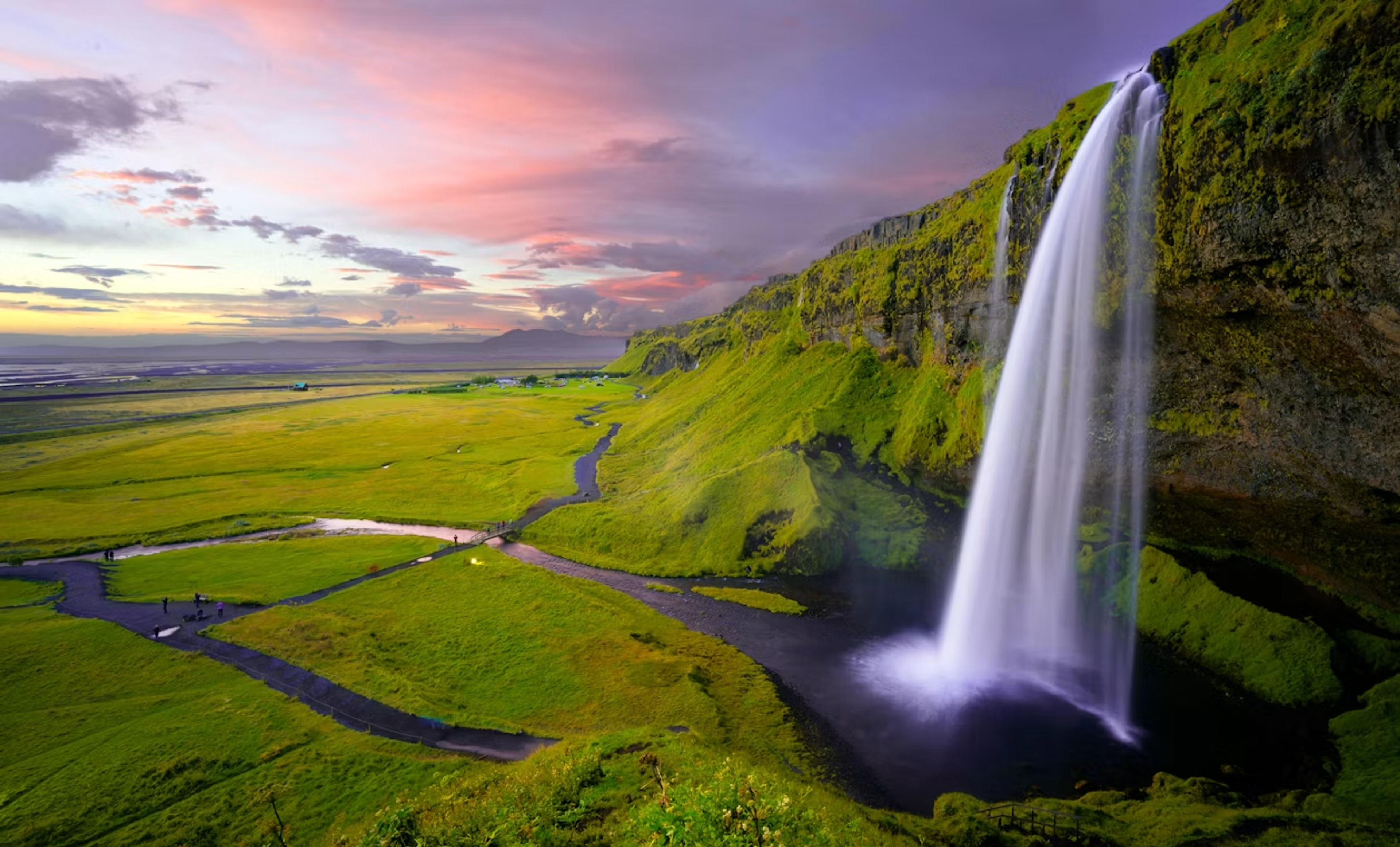 Seljalandsfoss waterfall cascades down a lush green cliffside against a vibrant sunset in Iceland.