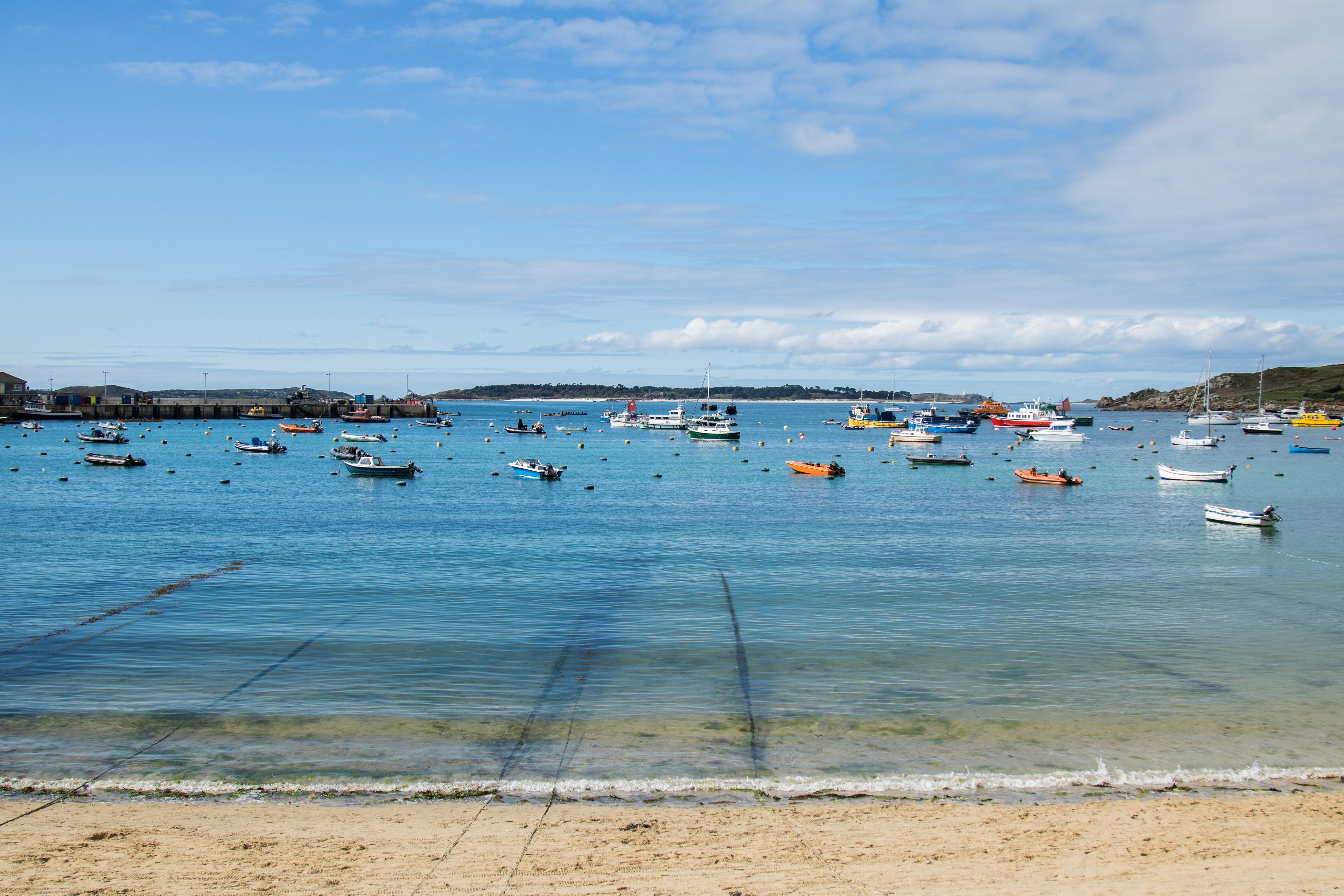 A collection of colorful boats floats on the clear waters of Hugh Town harbour on St Mary's in the Isles of Scilly.