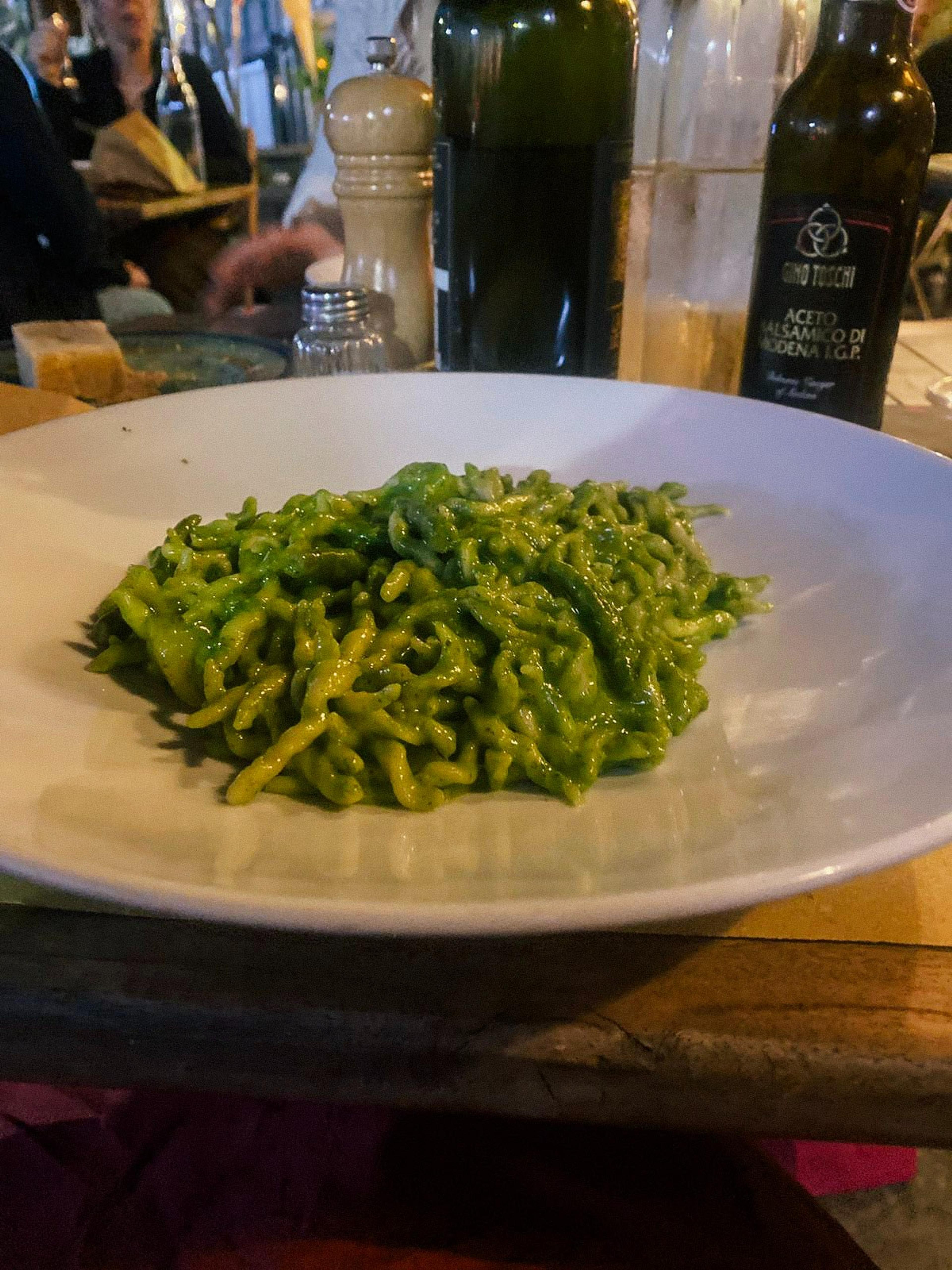 A plate of pasta with pesto sauce sits on a table at an outdoor restaurant