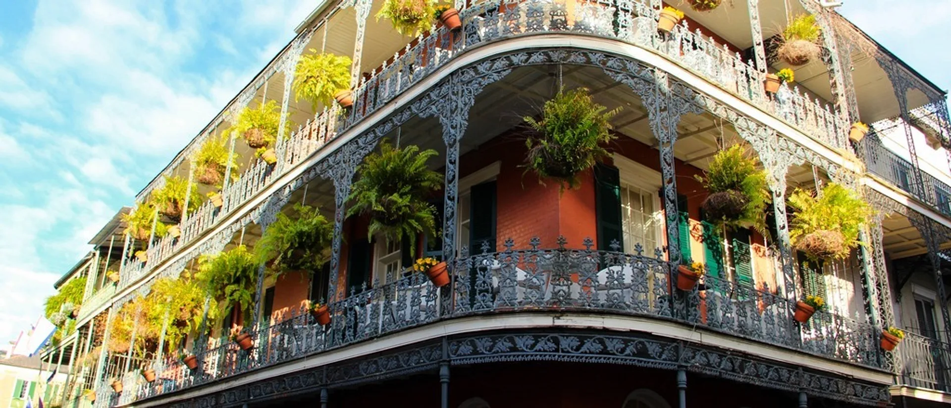 A historic building adorned with ornate wrought-iron balconies and lush hanging plants in the French Quarter of New Orleans.