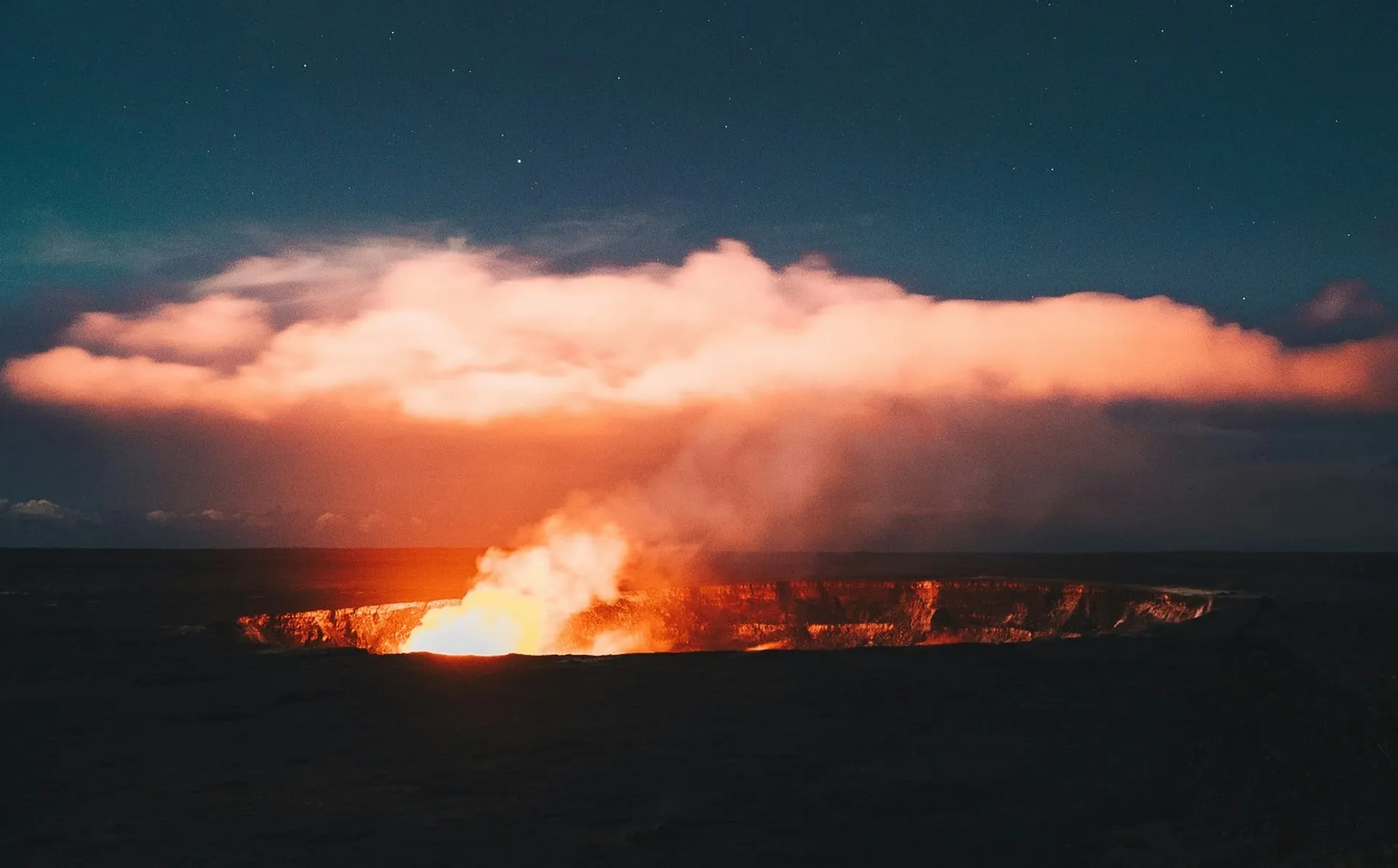 Molten lava glows within the Halemaʻumaʻu Crater at Kilauea Volcano in Hawaii, casting a fiery light against the night sky.