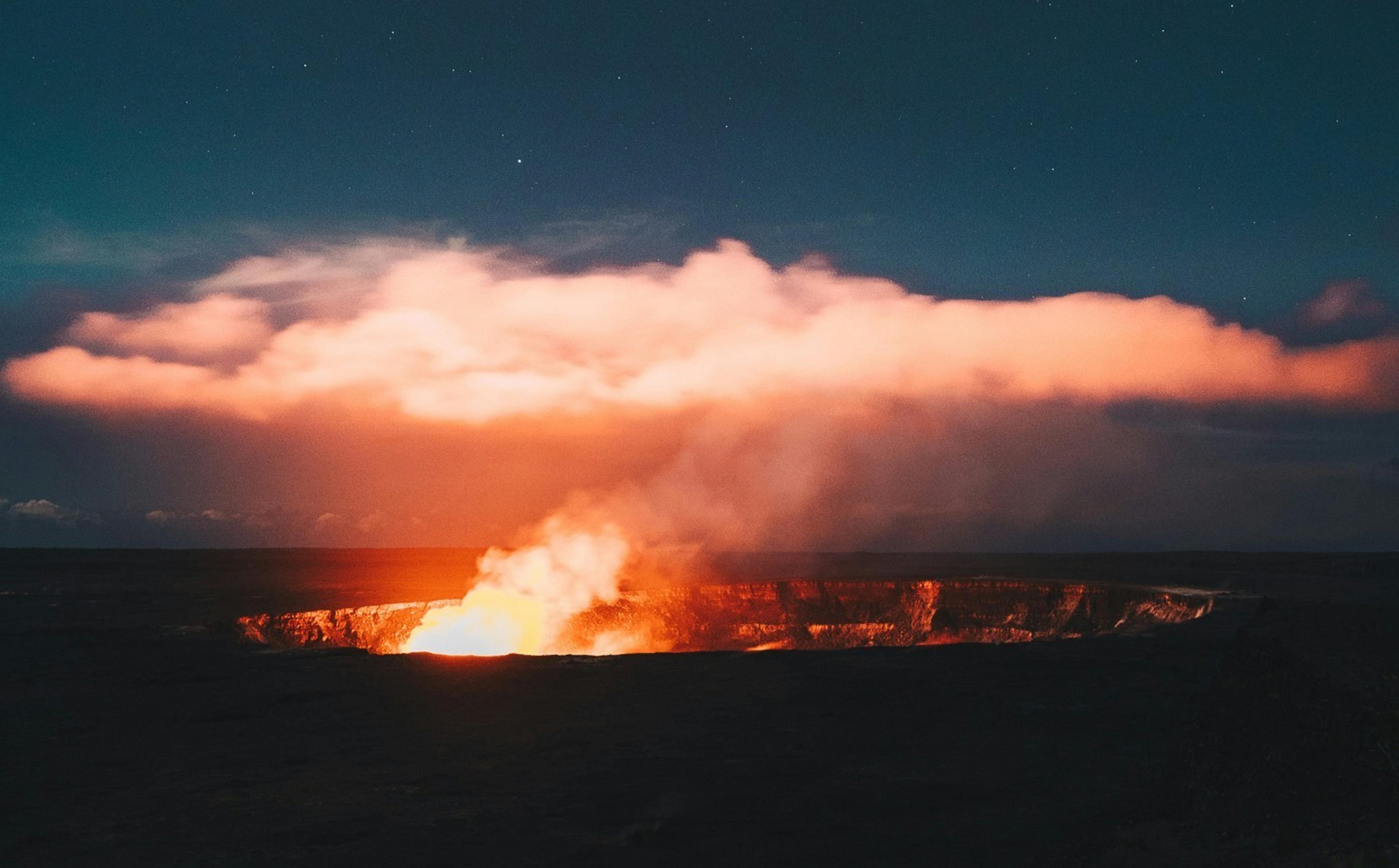 Molten lava glows within the Halemaʻumaʻu Crater at Kilauea Volcano in Hawaii, casting a fiery light against the night sky.