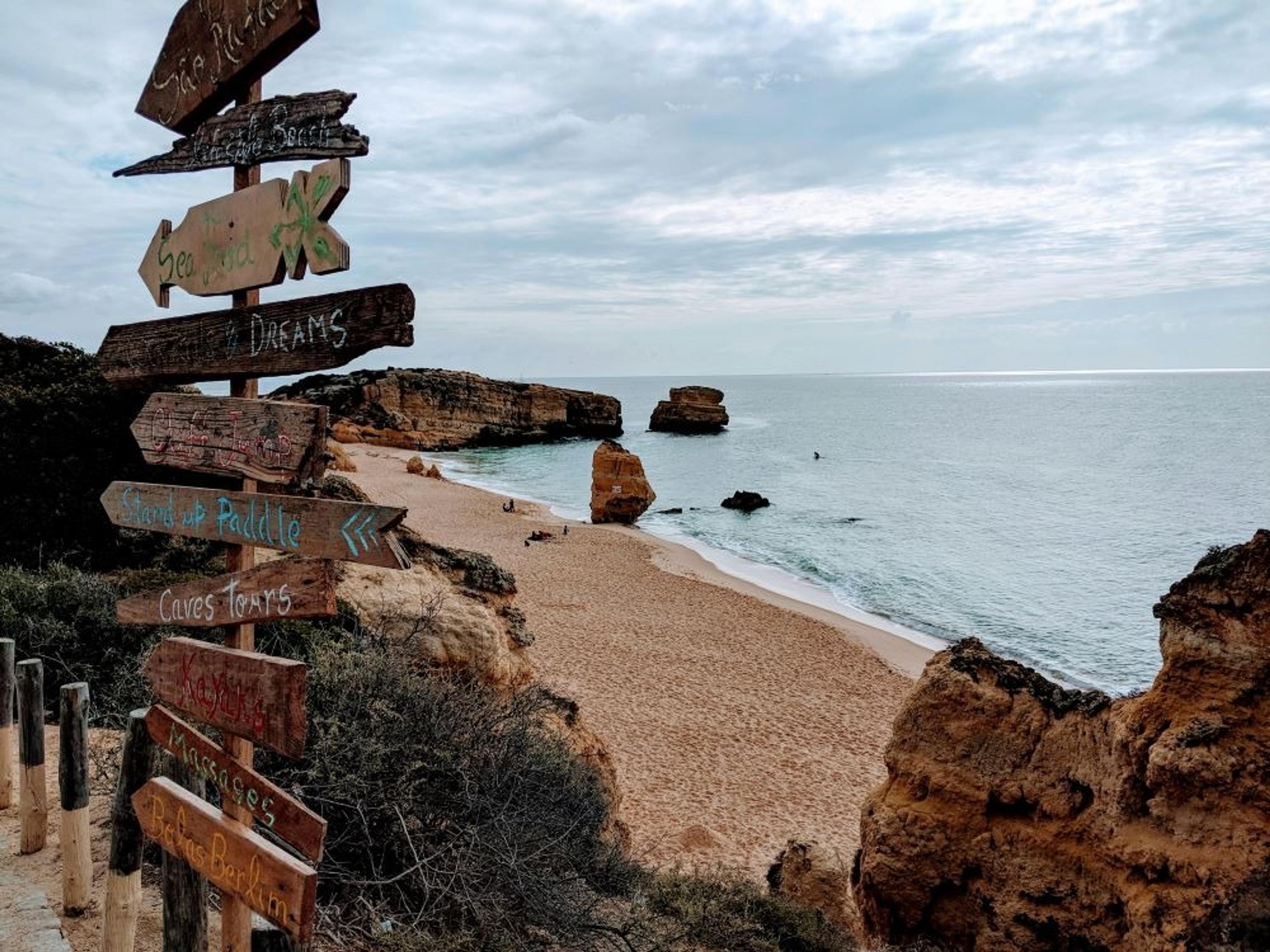 Wooden signs point to various activities overlooking the scenic coastline of Praia dos Tres Castelos in Portugal.