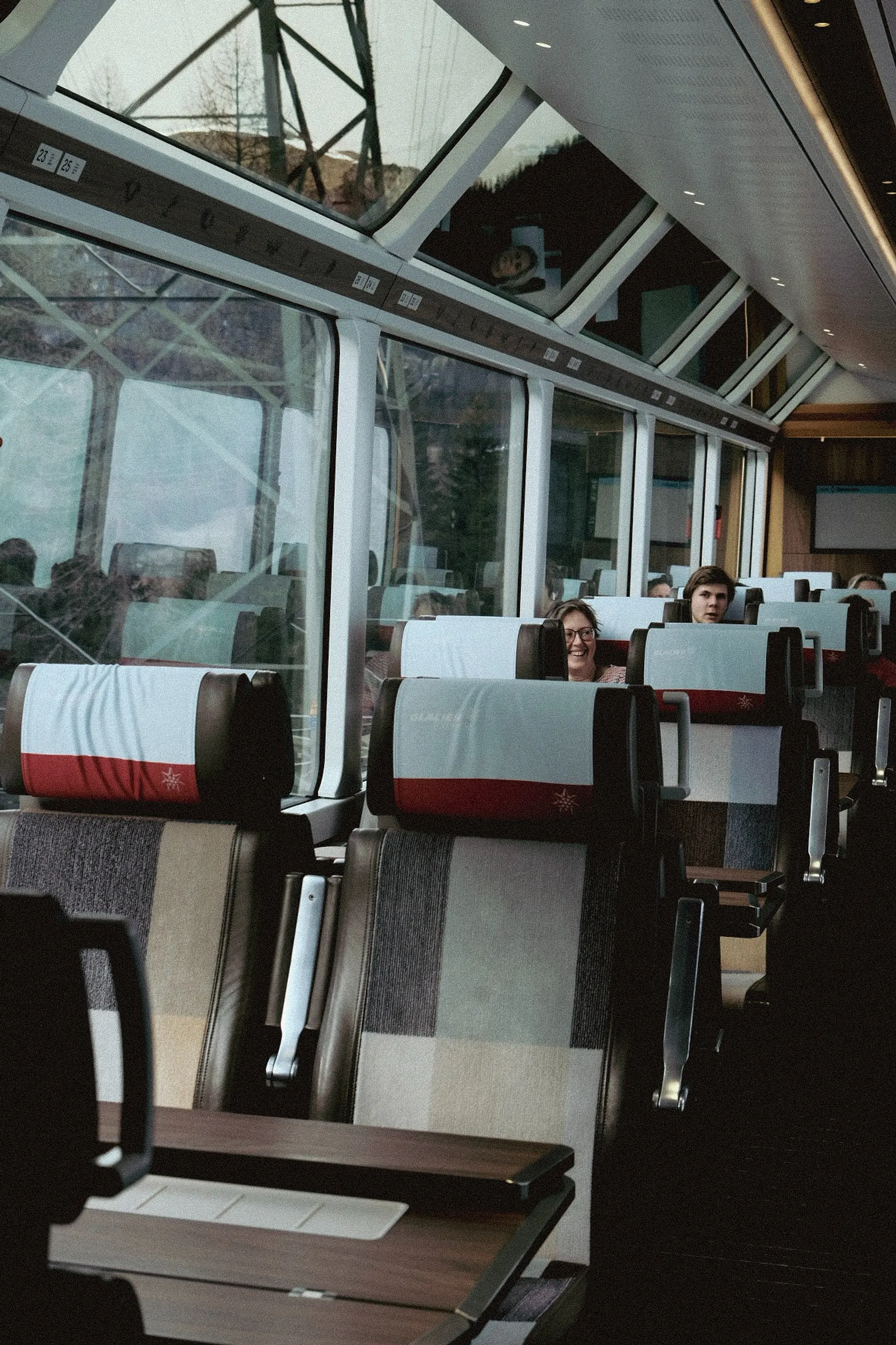Passengers enjoy the scenic views inside a Glacier Express train in Switzerland, characterized by its large panoramic windows.