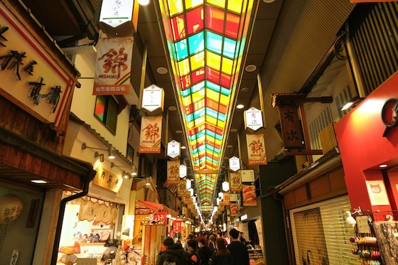 A bustling Nishiki Market in Kyoto, with vibrant stained glass ceiling and numerous shops lining the arcade.