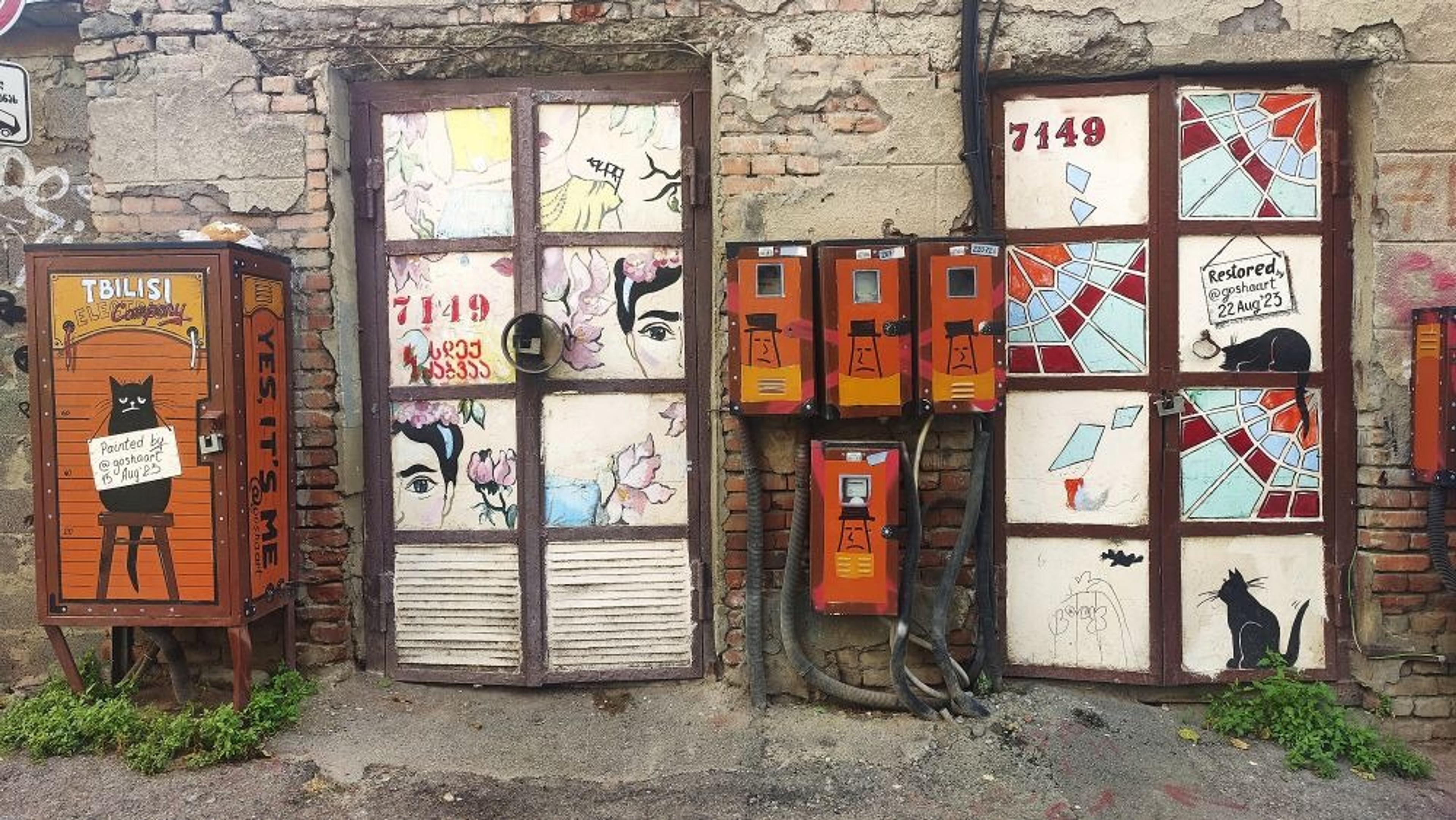 Colorful street art featuring cats and abstract designs adorns a brick wall, marked as a creation from Tbilisi.