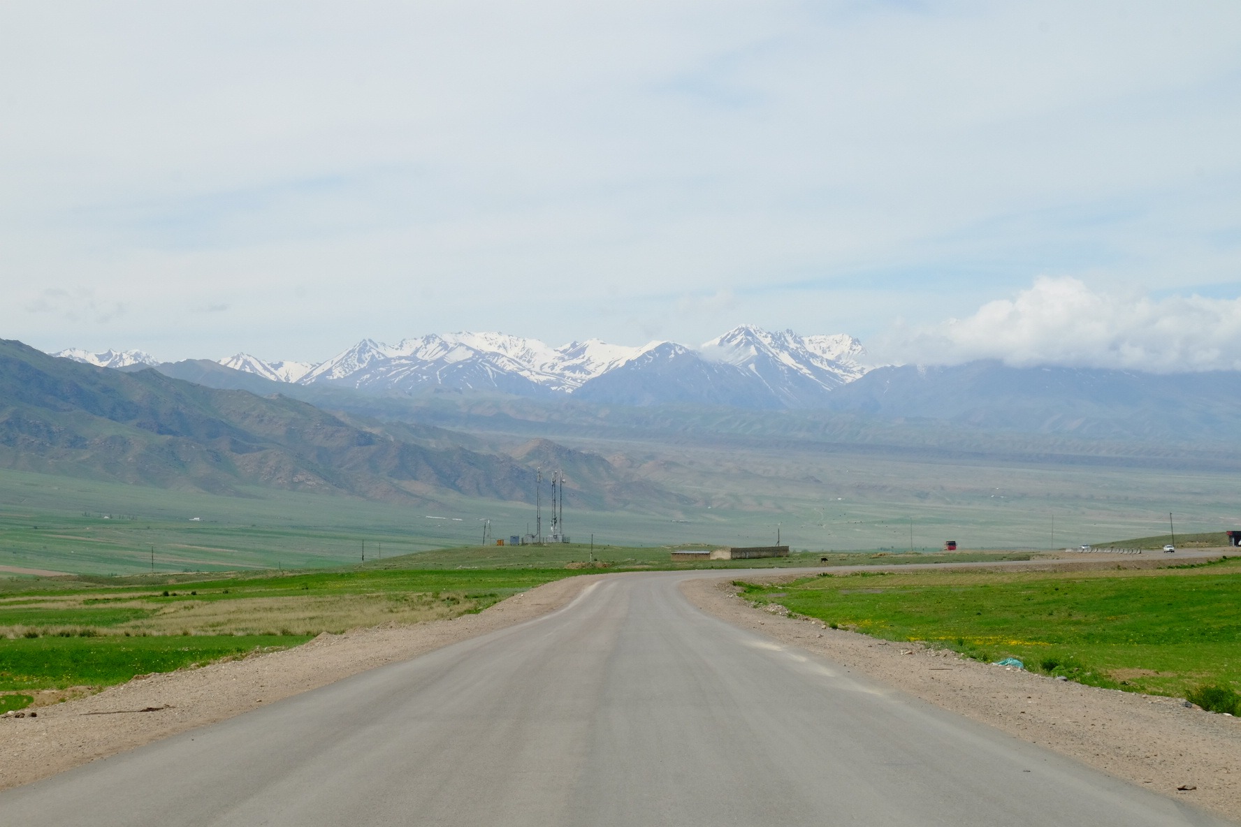 A rural road stretches towards the snow-capped peaks of the Kyrgyz Ala-Too Range in Kyrgyzstan.