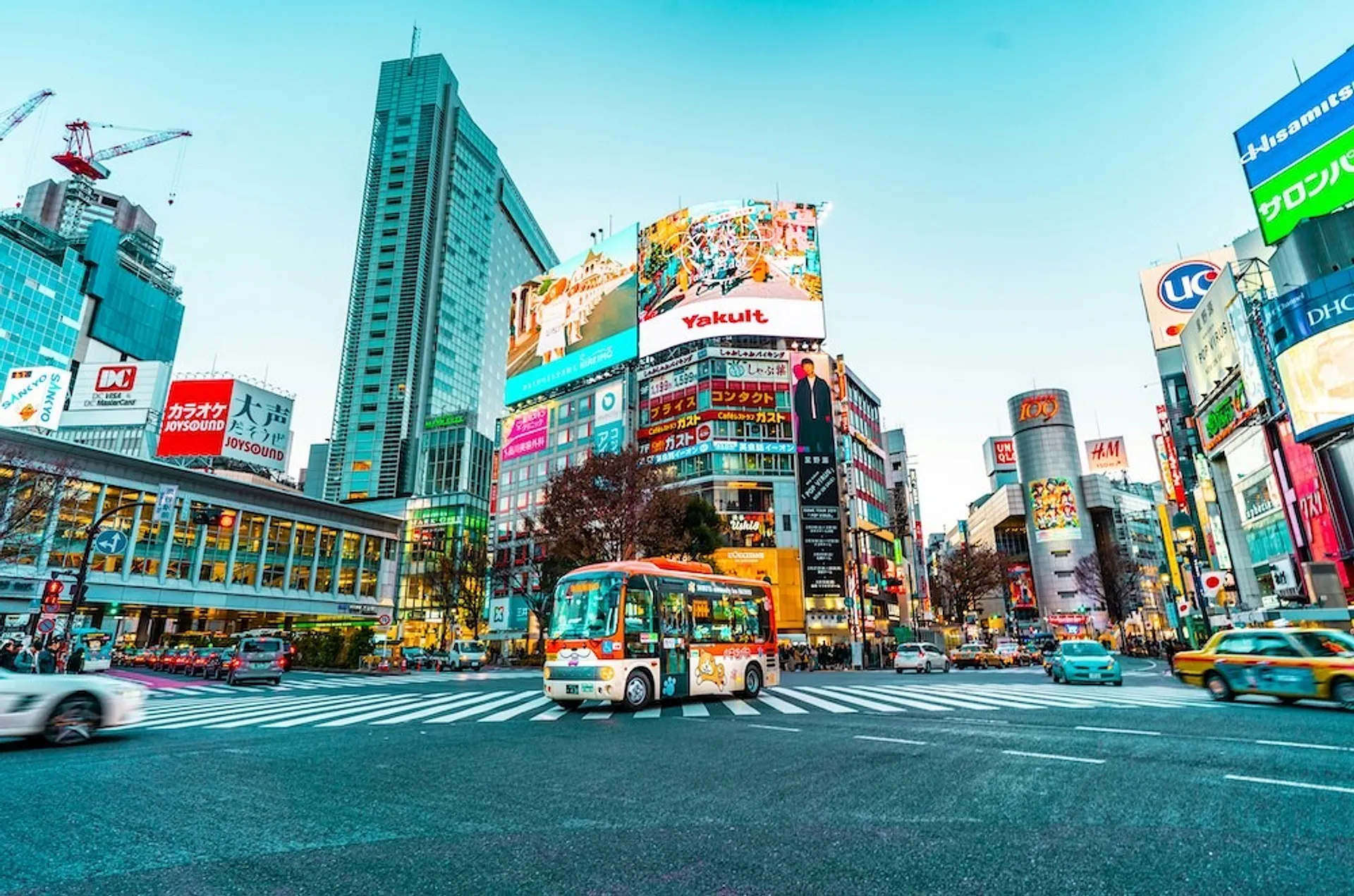 A bustling scene at the iconic Shibuya Crossing in Tokyo, Japan, with vibrant billboards and streams of vehicles and pedestrians.