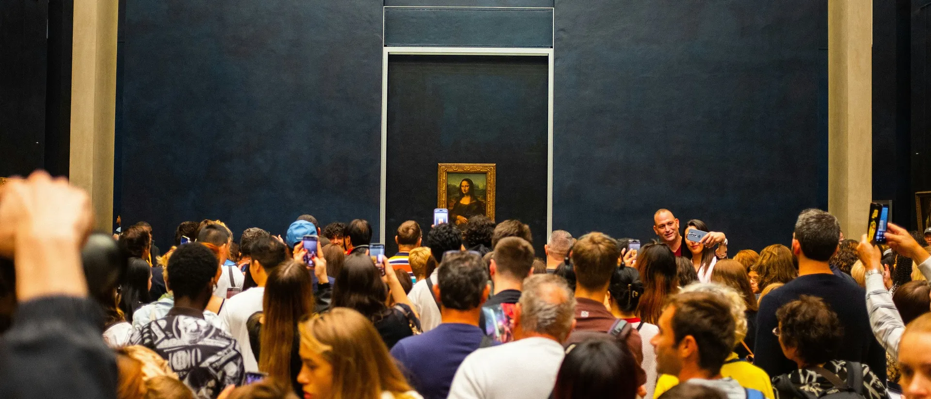 Visitors gather around the "Mona Lisa" painting in the Louvre Museum, Paris, capturing the iconic artwork on their smartphones.