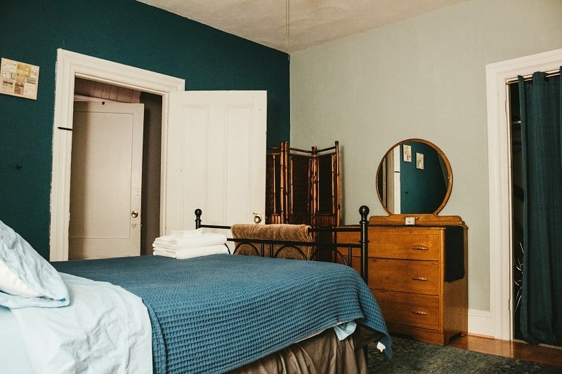 Bedroom with green walls, a bed, round mirror and drawers