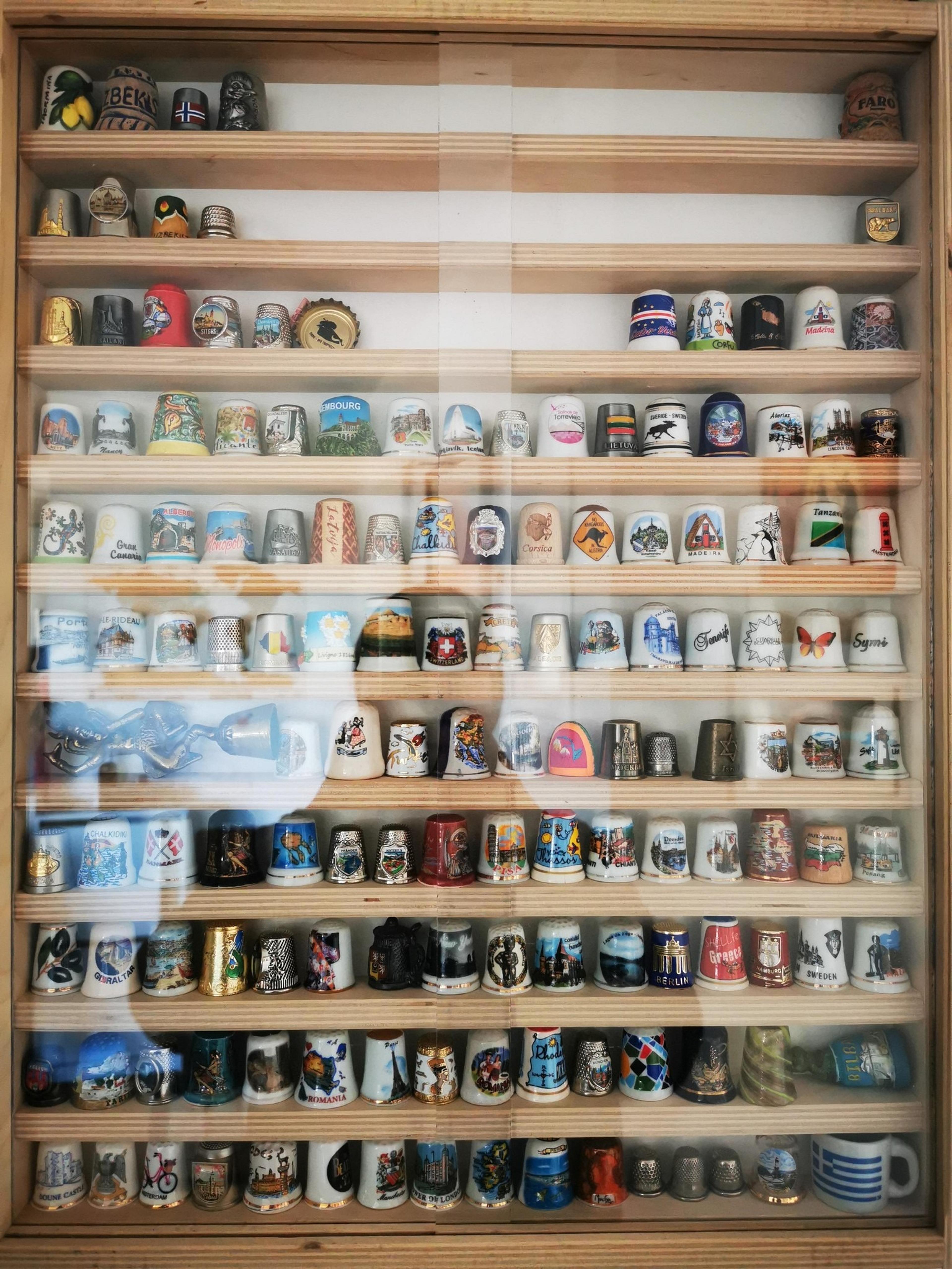 A display case filled with souvenir thimbles, each representing different locations around the world, including Berlin and Crete.