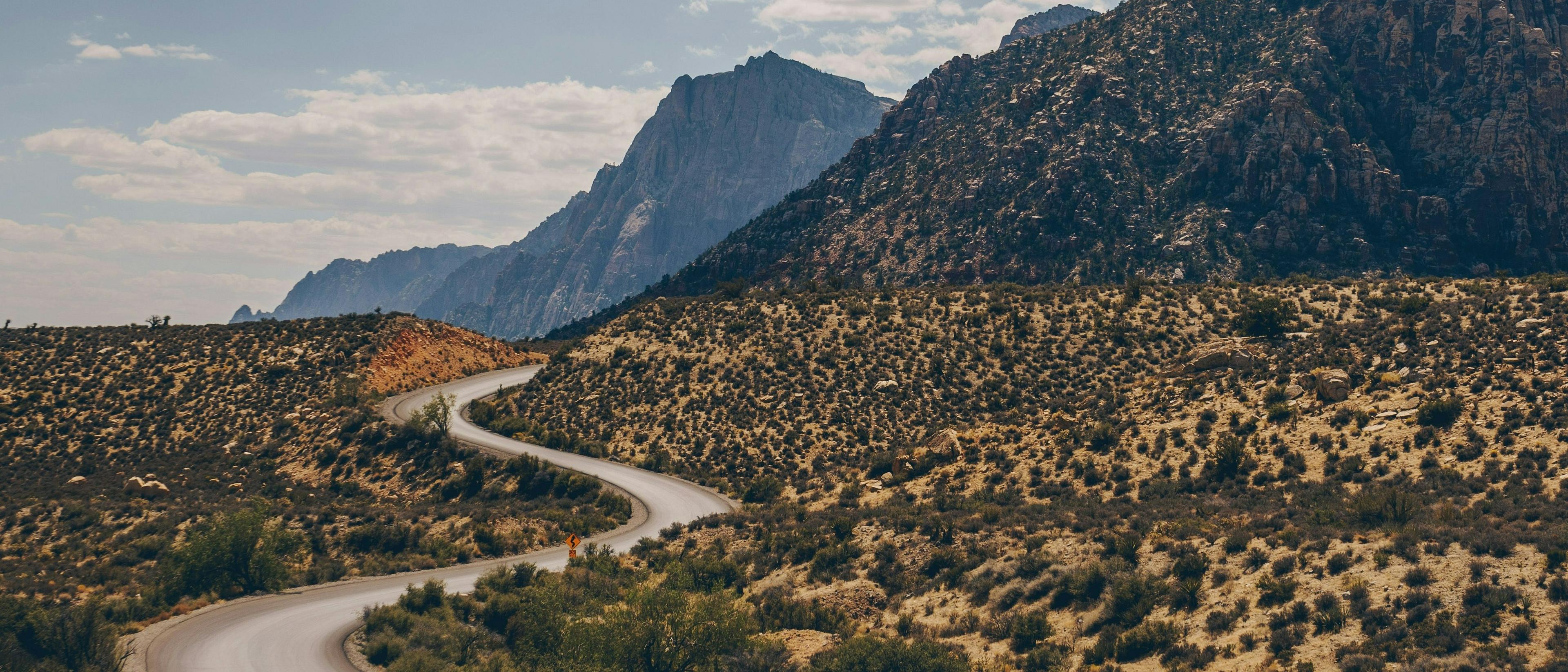 A winding road curves through the desert landscape of Red Rock Canyon, Nevada, with rugged mountains in the background.