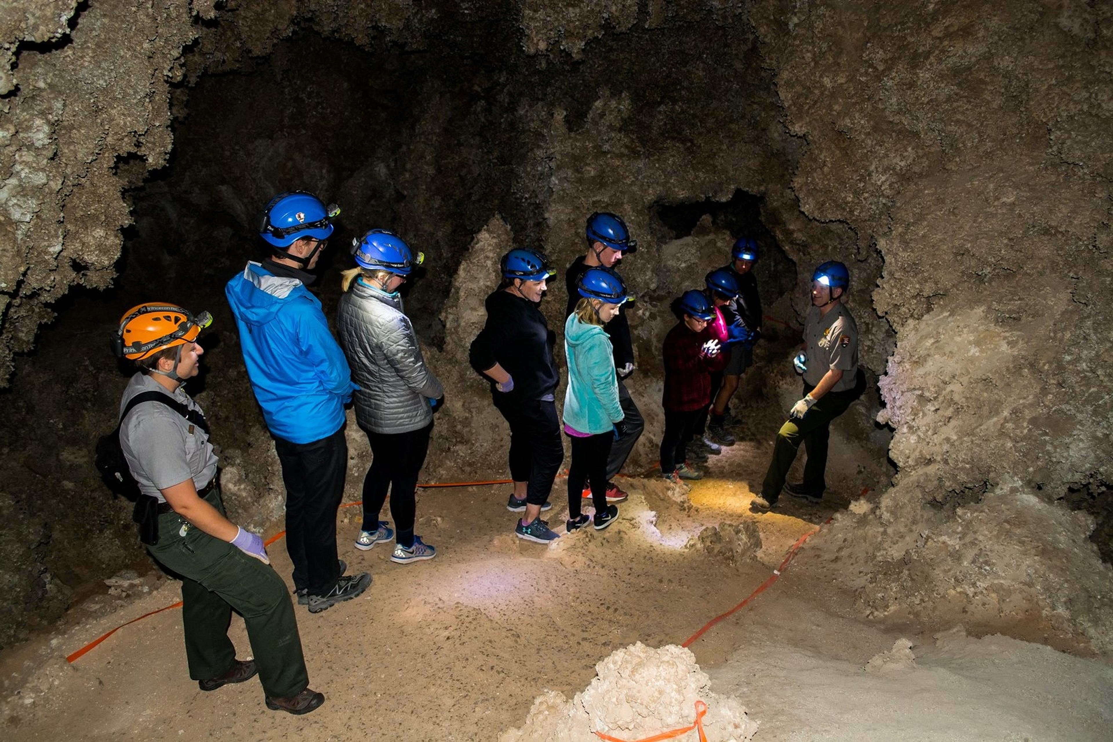 A group of people wearing helmets and headlamps explores a cave with a guide at Carlsbad Caverns National Park.