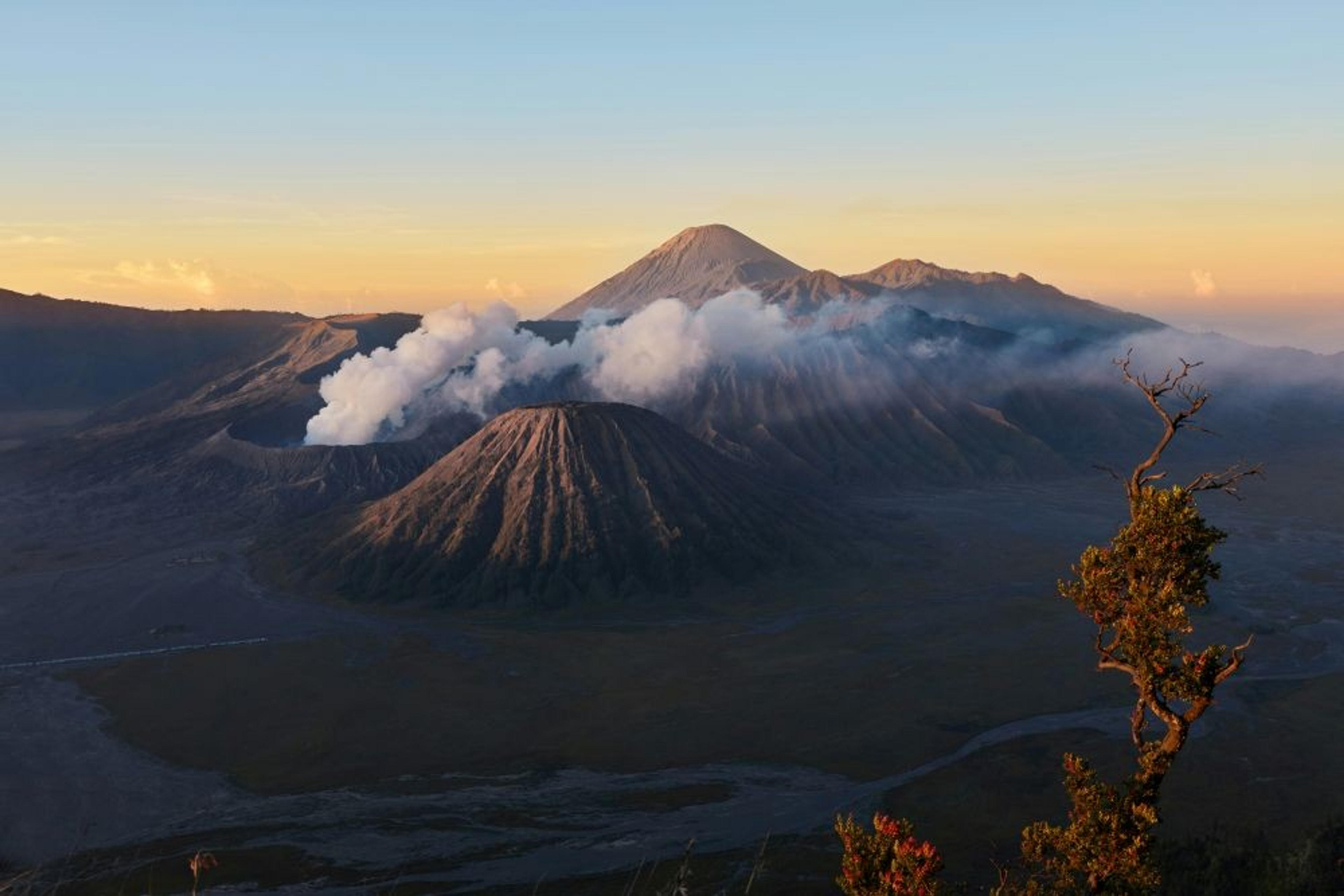 Mount Bromo in East Java, Indonesia, emits smoke under a clear dawn sky.