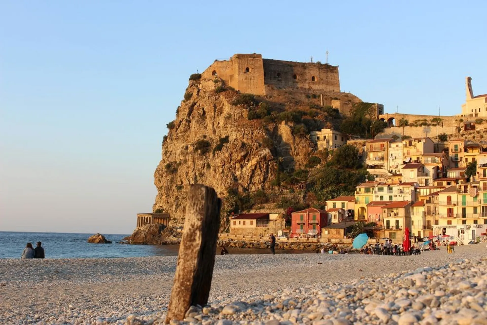 A scenic view of the beach beneath Castello Ruffo di Scilla in Calabria, Italy, with colorful houses lining the waterfront.