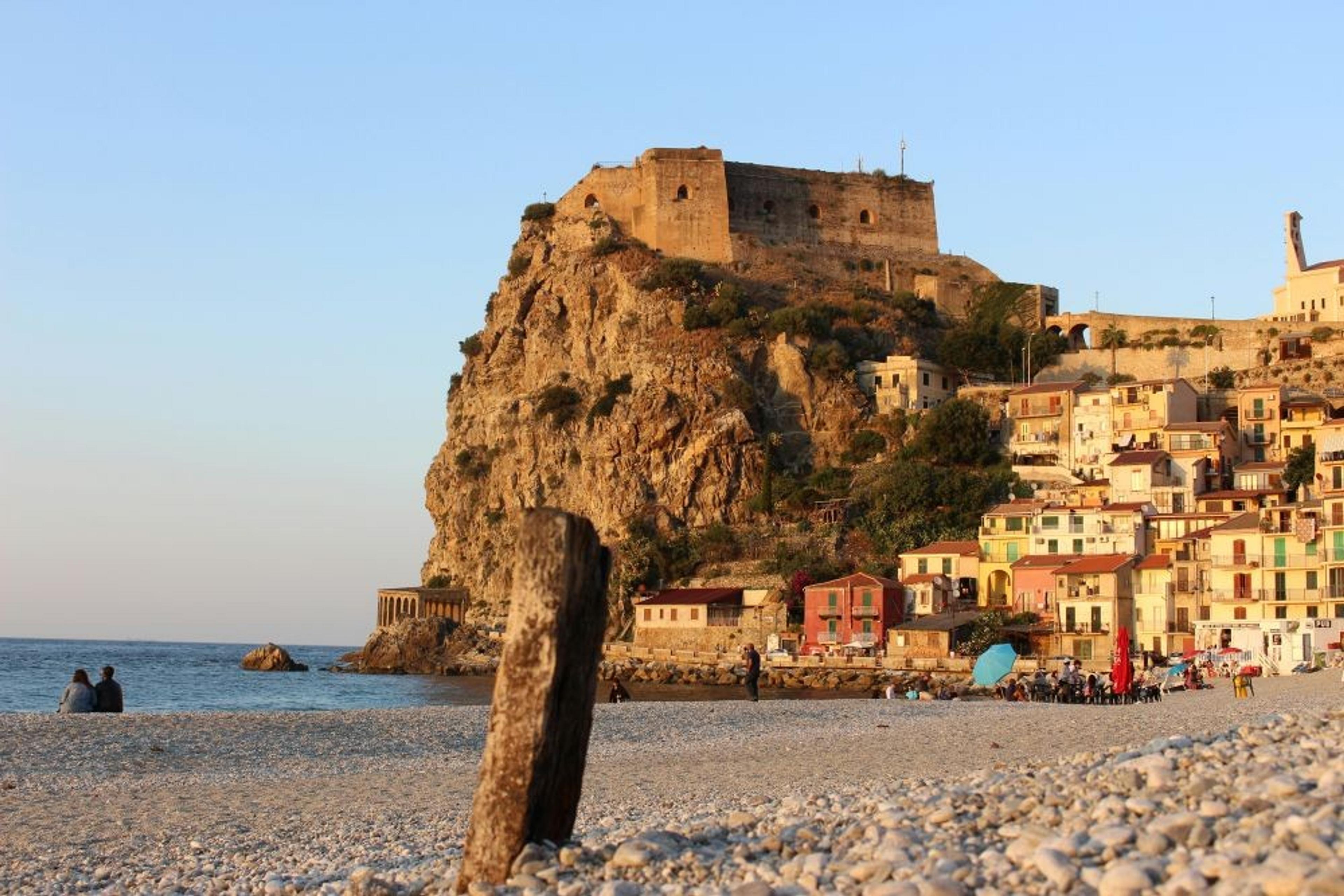 A scenic view of the beach beneath Castello Ruffo di Scilla in Calabria, Italy, with colorful houses lining the waterfront.