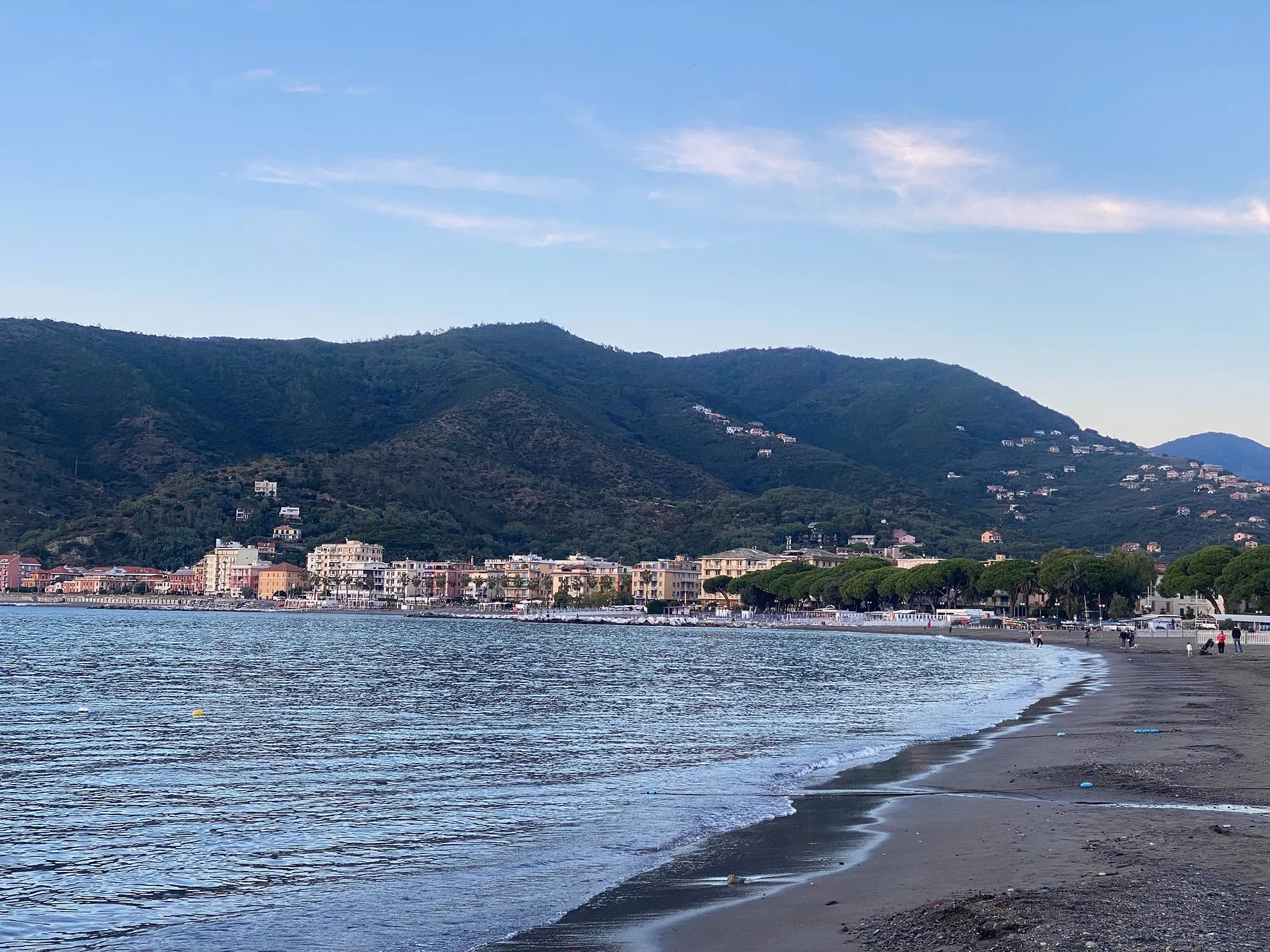 A beach in Italy features a picturesque coastline with distant green hills and charming seaside buildings.