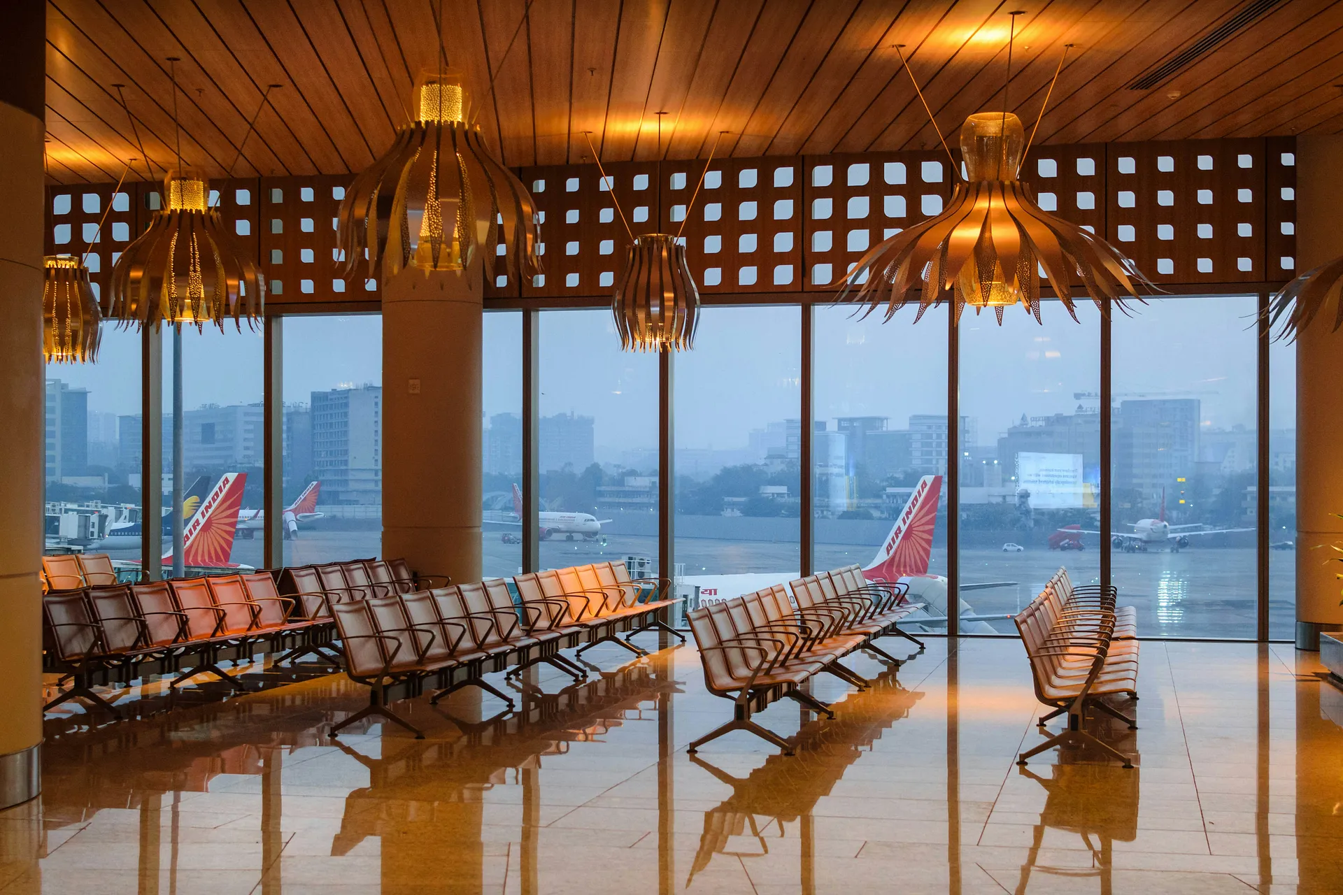 A tranquil view of the departure lounge at Chhatrapati Shivaji Maharaj International Airport in Mumbai, featuring Air India planes on the tarmac outside large windows.