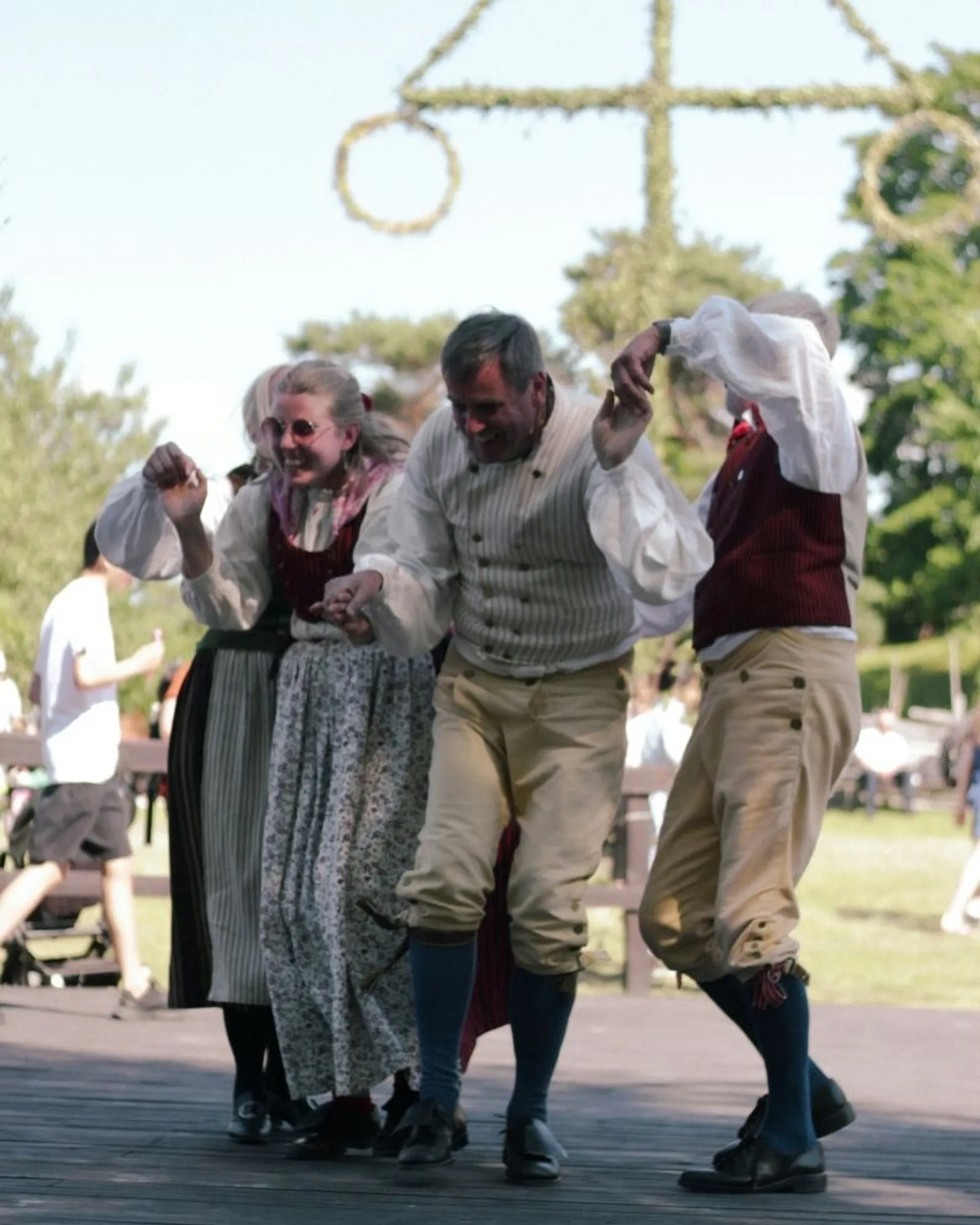 People in traditional Swedish attire dance joyfully at a midsummer celebration.
