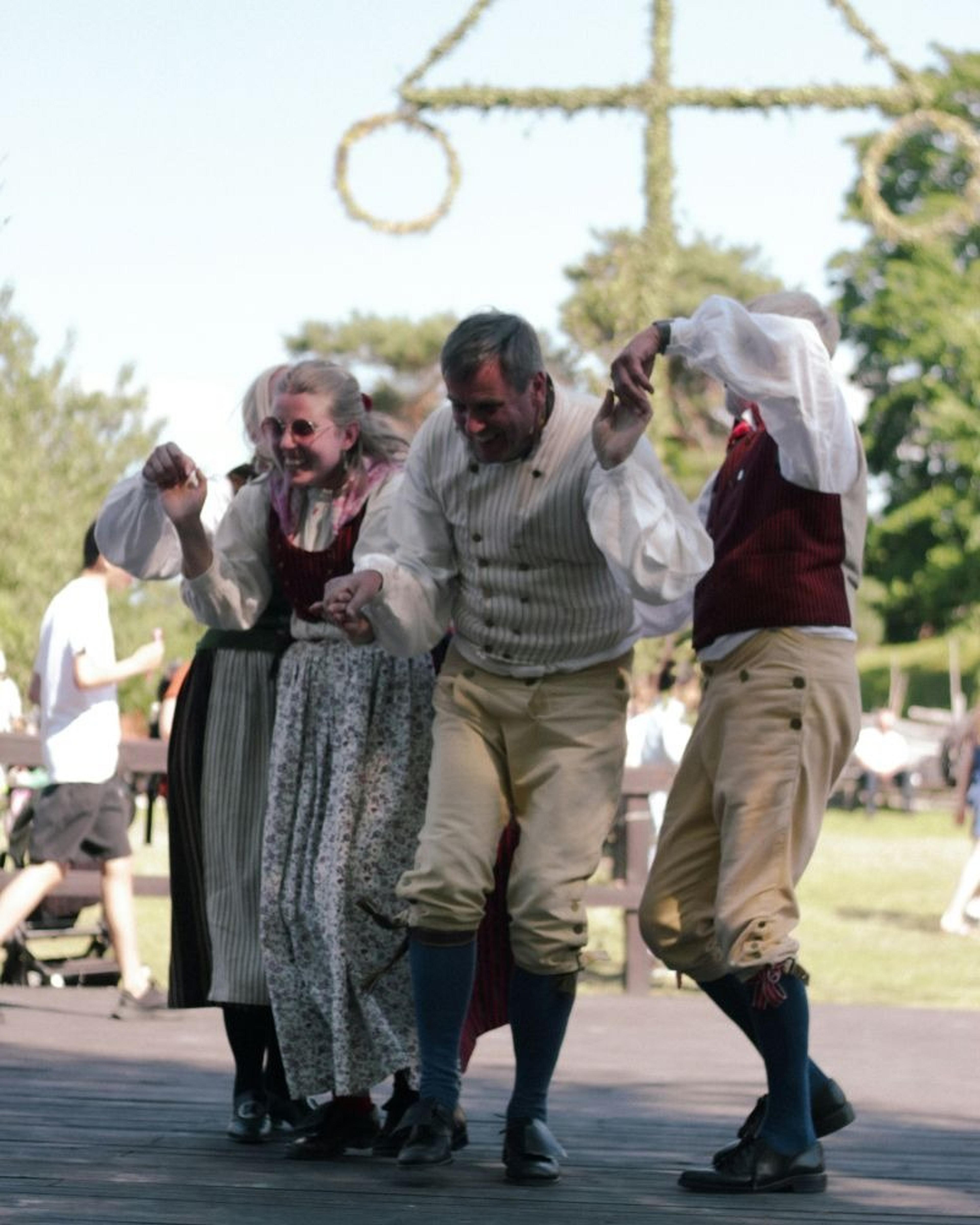 People in traditional Swedish attire dance joyfully at a midsummer celebration.