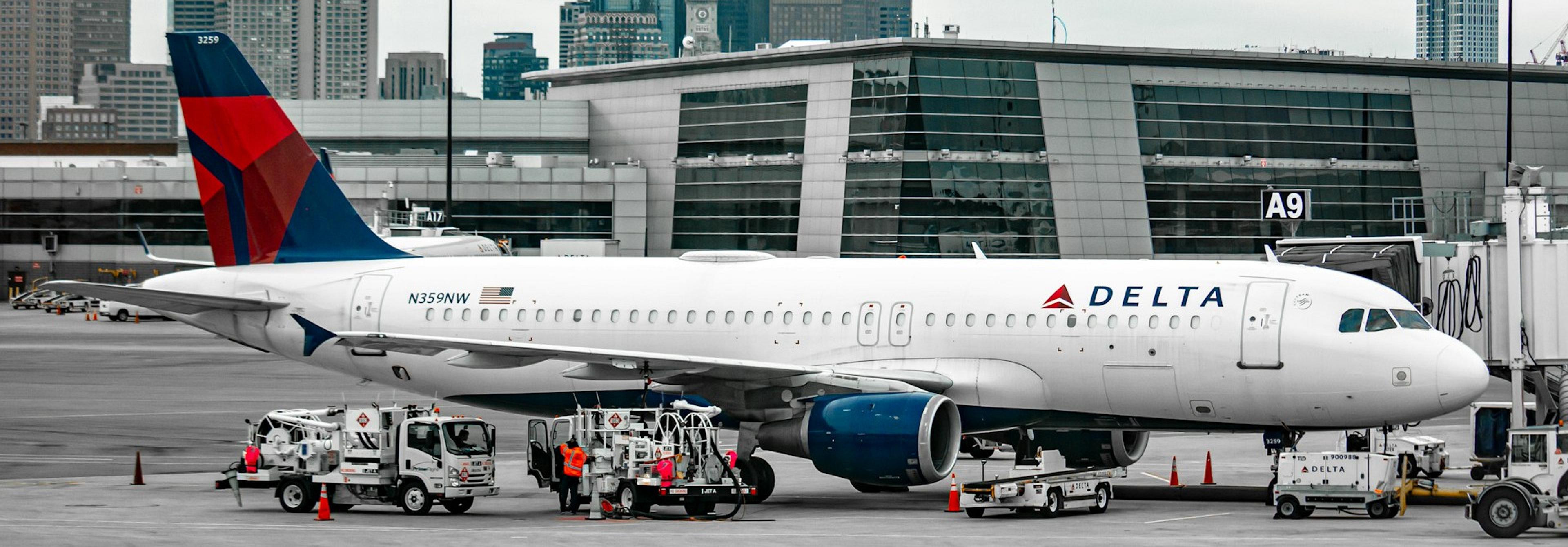 A Delta Air Lines aircraft is parked at Gate A9 at Logan International Airport in Boston, with the city skyline in the background.
