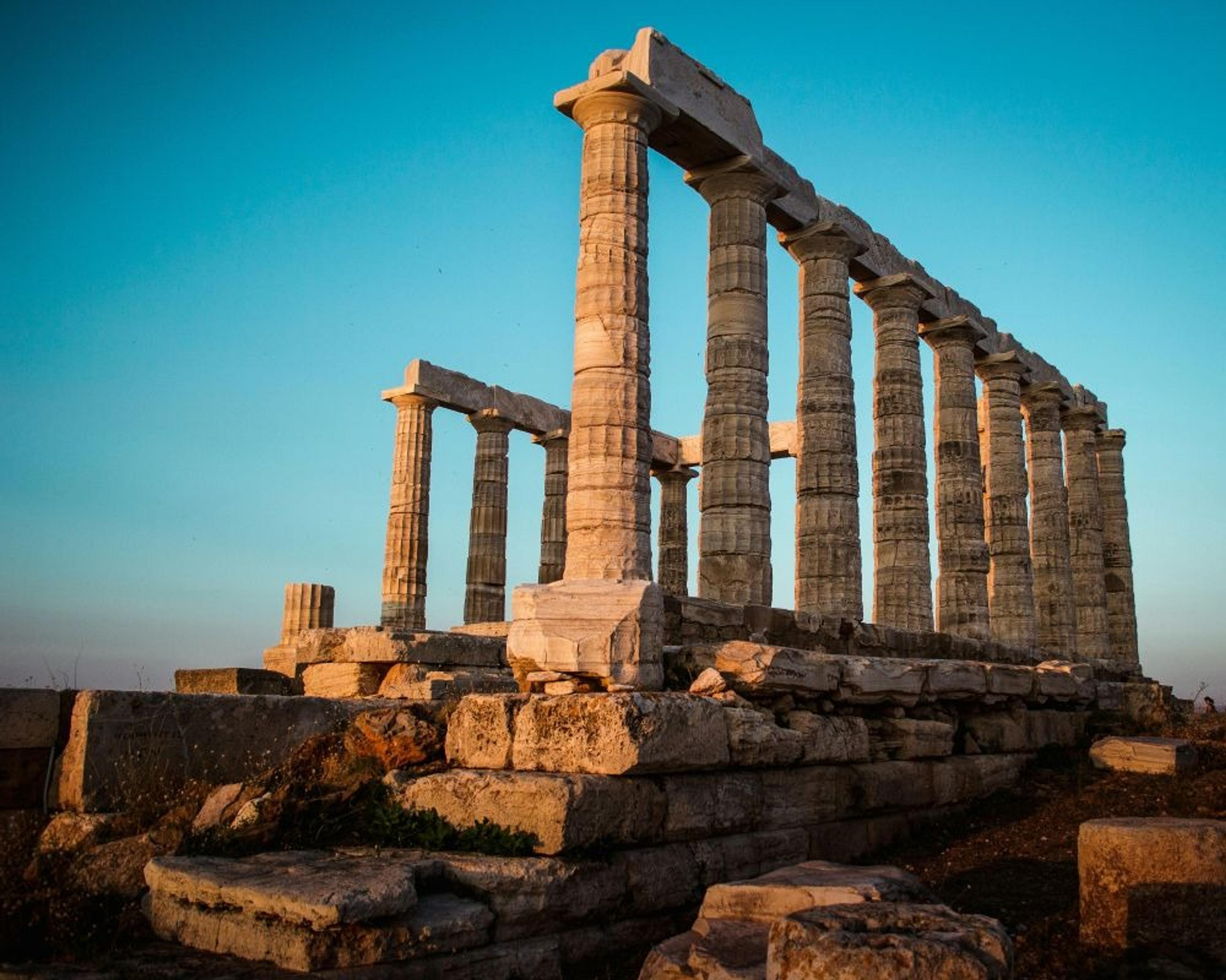 Ancient Doric columns of the Temple of Poseidon stand majestically at Cape Sounion under a clear blue sky.