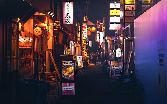 A vibrant narrow alley in Kyoto illuminated by colorful neon signs and lanterns.