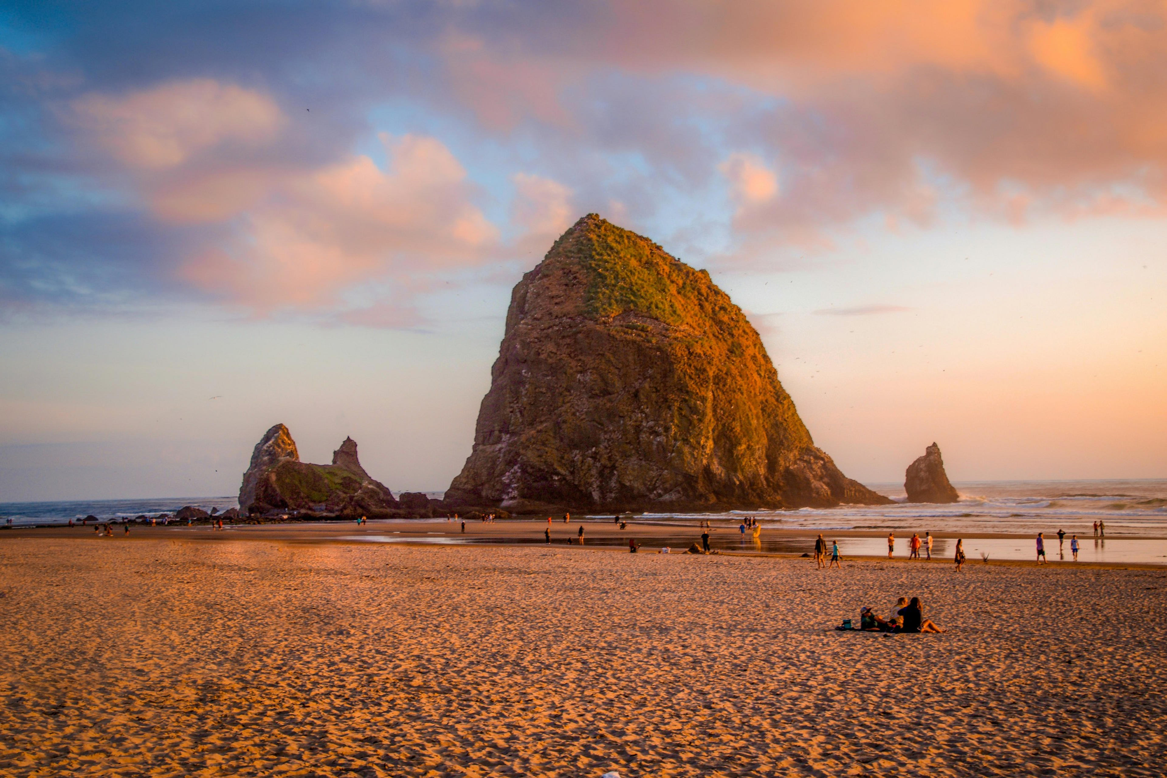 People gather on the sandy shores of Cannon Beach, Oregon, admiring the iconic Haystack Rock at sunset.
