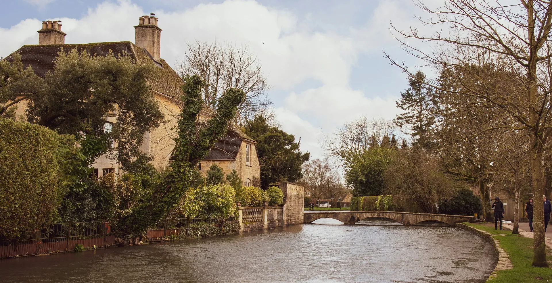 A picturesque stone cottage and arched bridge beside the tranquil River Windrush in Bourton-on-the-Water, England.