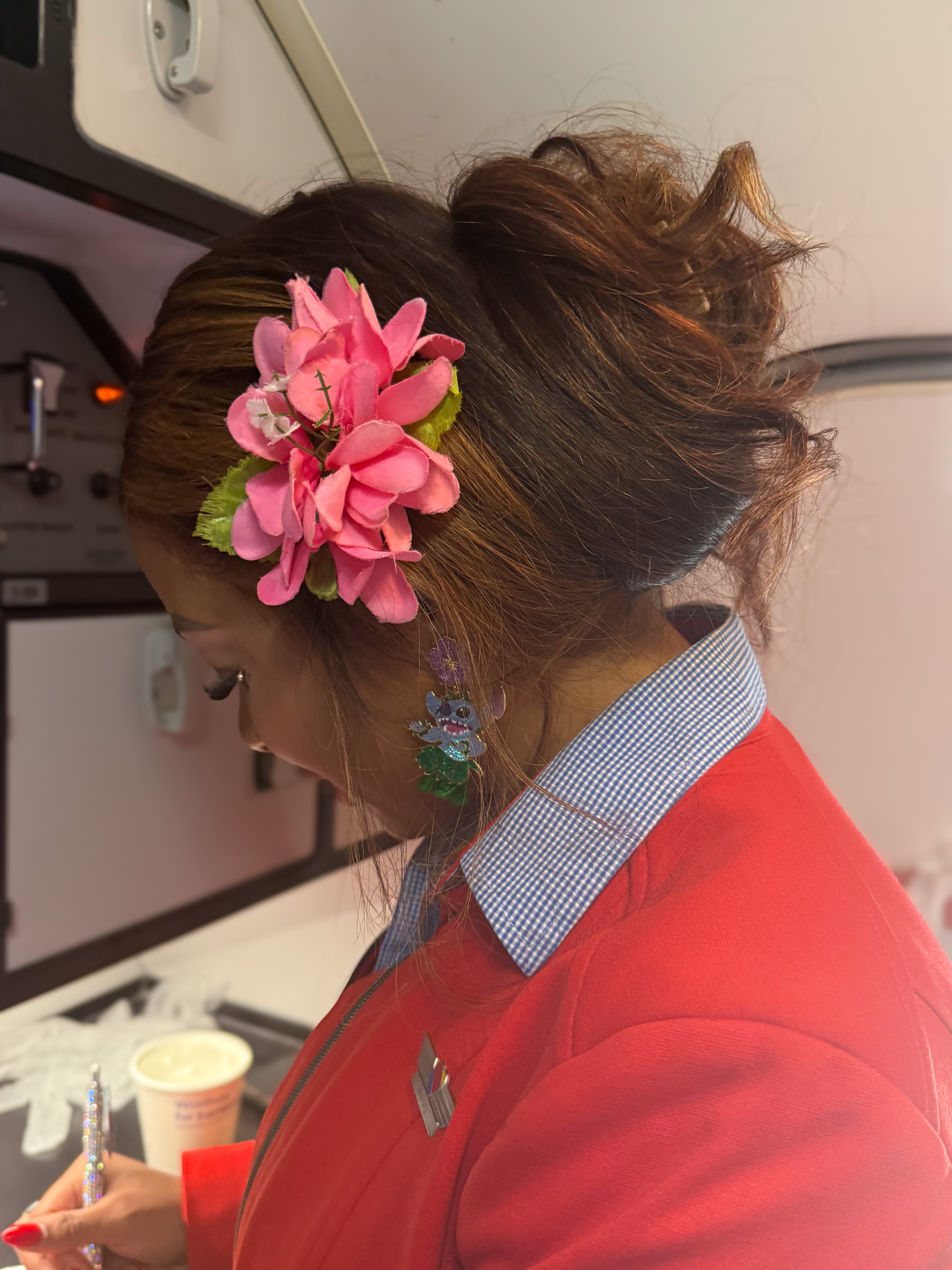 A flight attendant, adorned with a pink flower in her hair, writes inside an airplane galley.