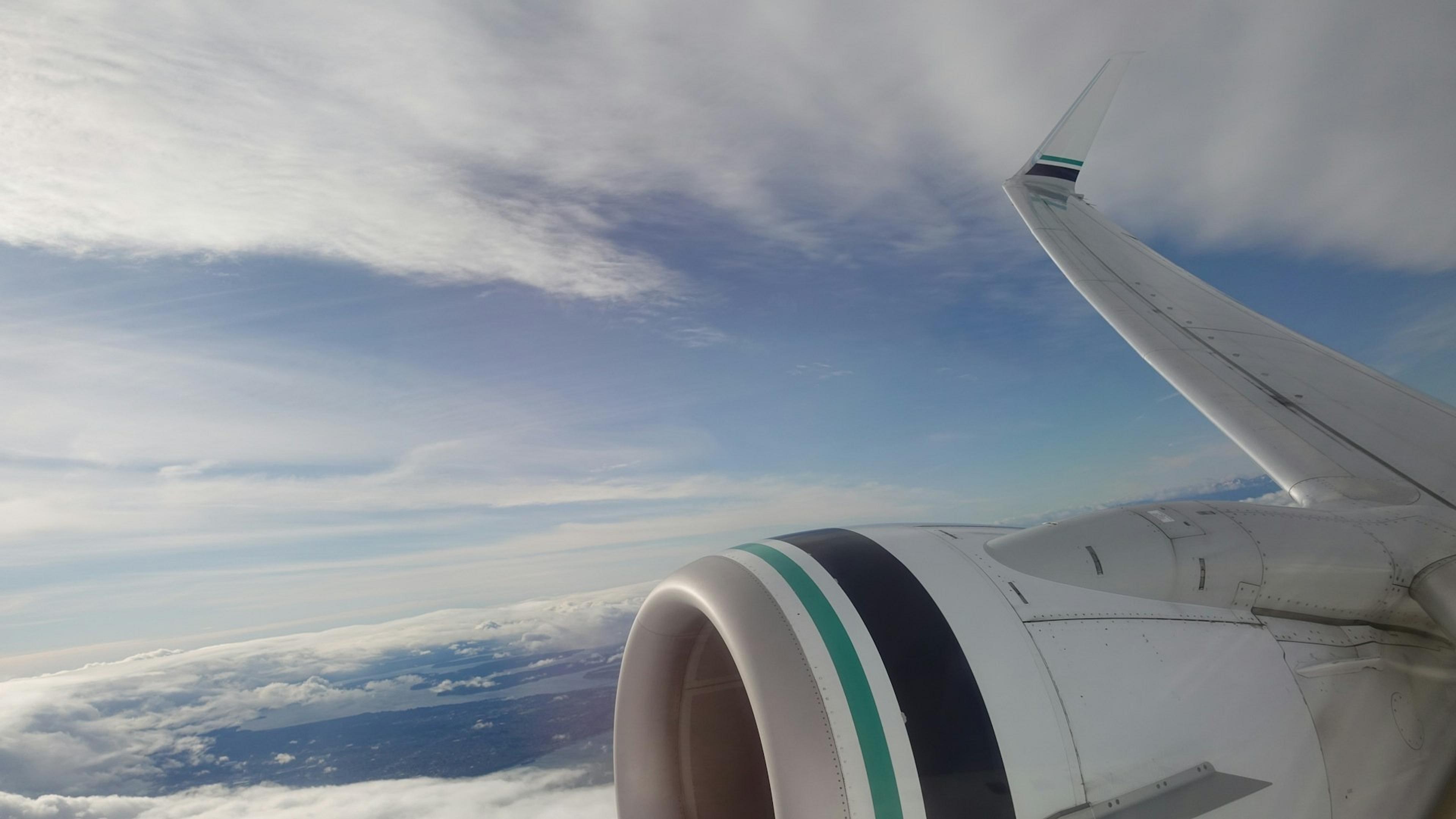 An airplane wing with Alaska Airlines' signature design soars above the clouds.