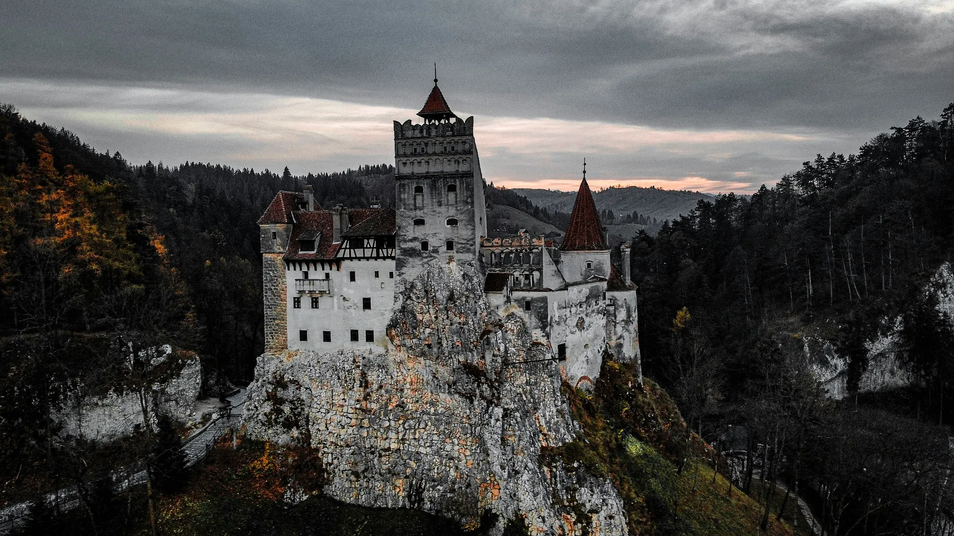 Bran Castle in Transylvania stands majestically on a rocky outcrop, surrounded by dense forests under a moody sky.