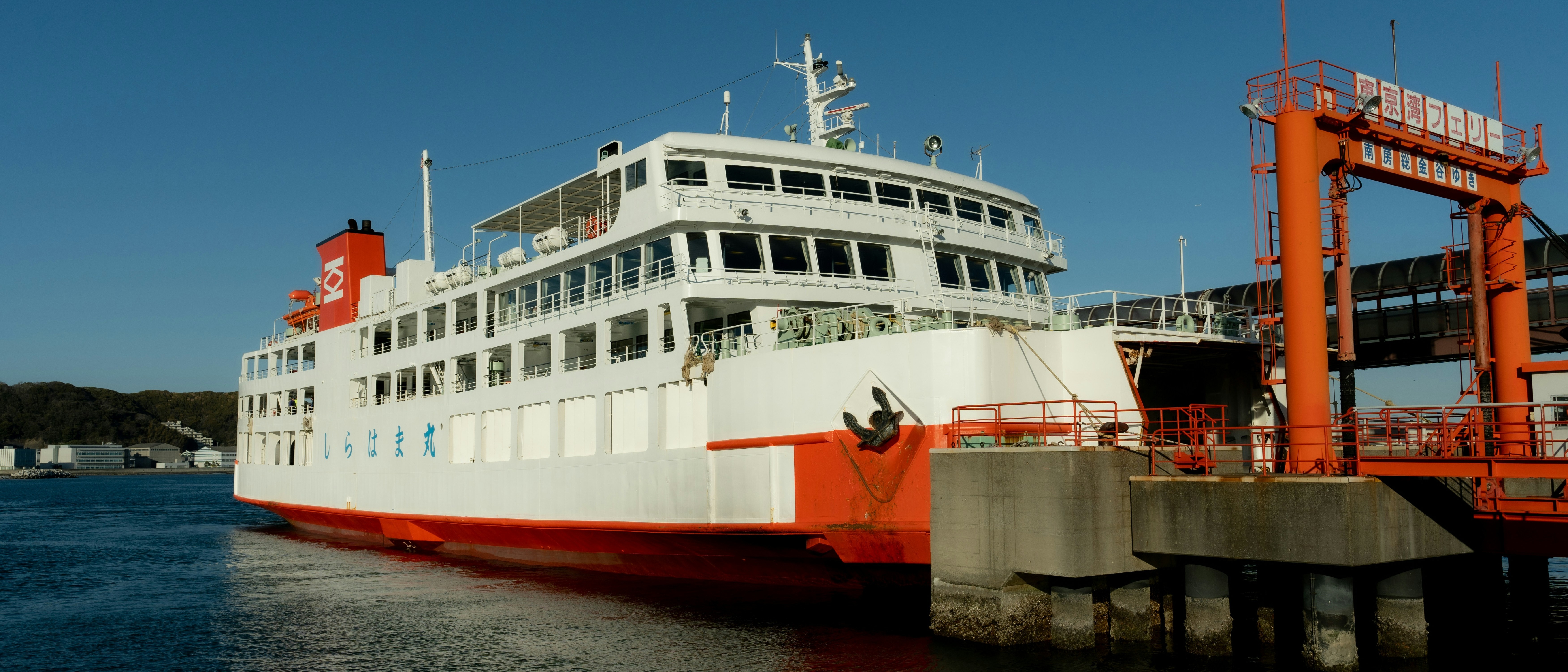 A ferry docks at the terminal in Tokyo Bay, Japan, with distinctive Japanese signage and coastal landscape in the background.