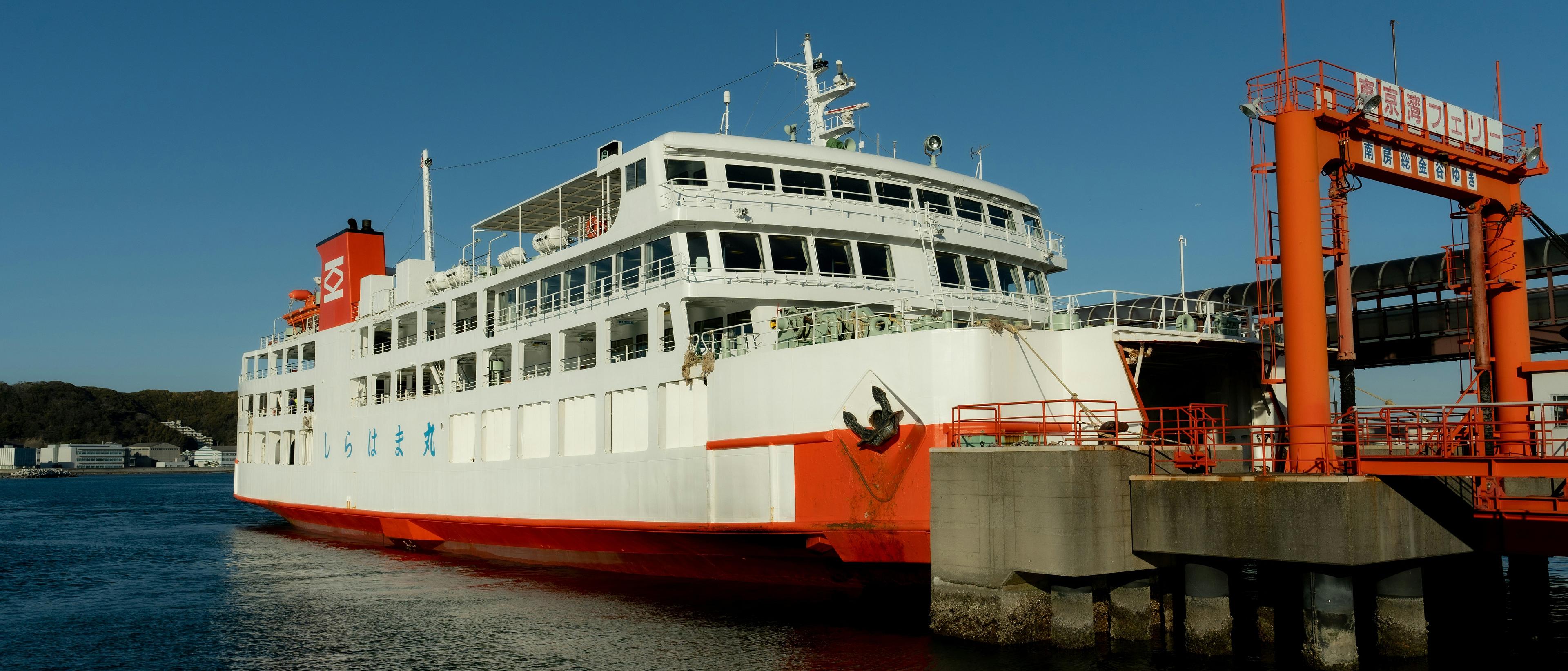 A ferry docks at the terminal in Tokyo Bay, Japan, with distinctive Japanese signage and coastal landscape in the background.