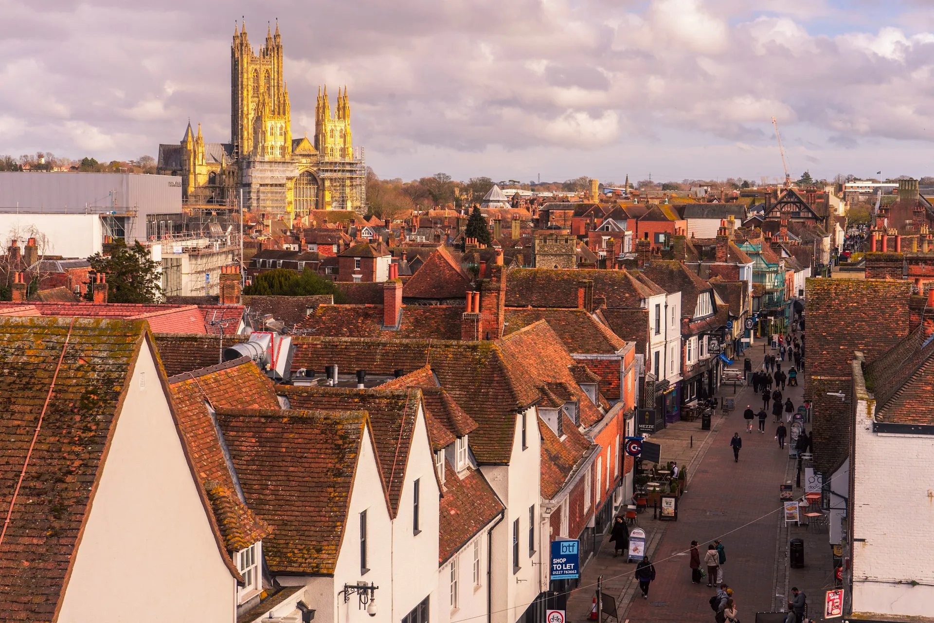 A picturesque view of Canterbury, England, features the iconic Canterbury Cathedral towering above a charming street lined with historic buildings.