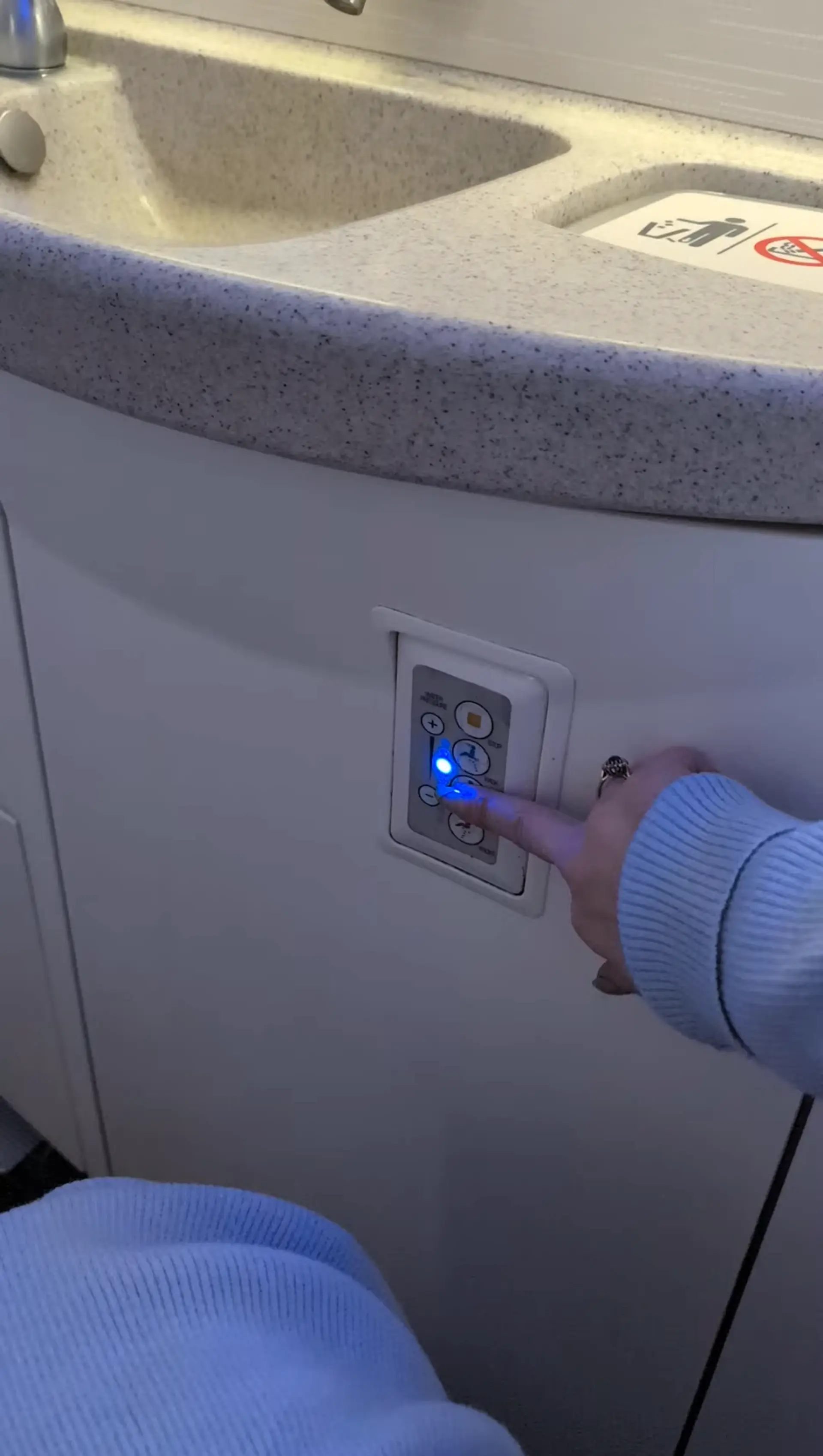 A person presses a button on a panel in an airplane lavatory.
