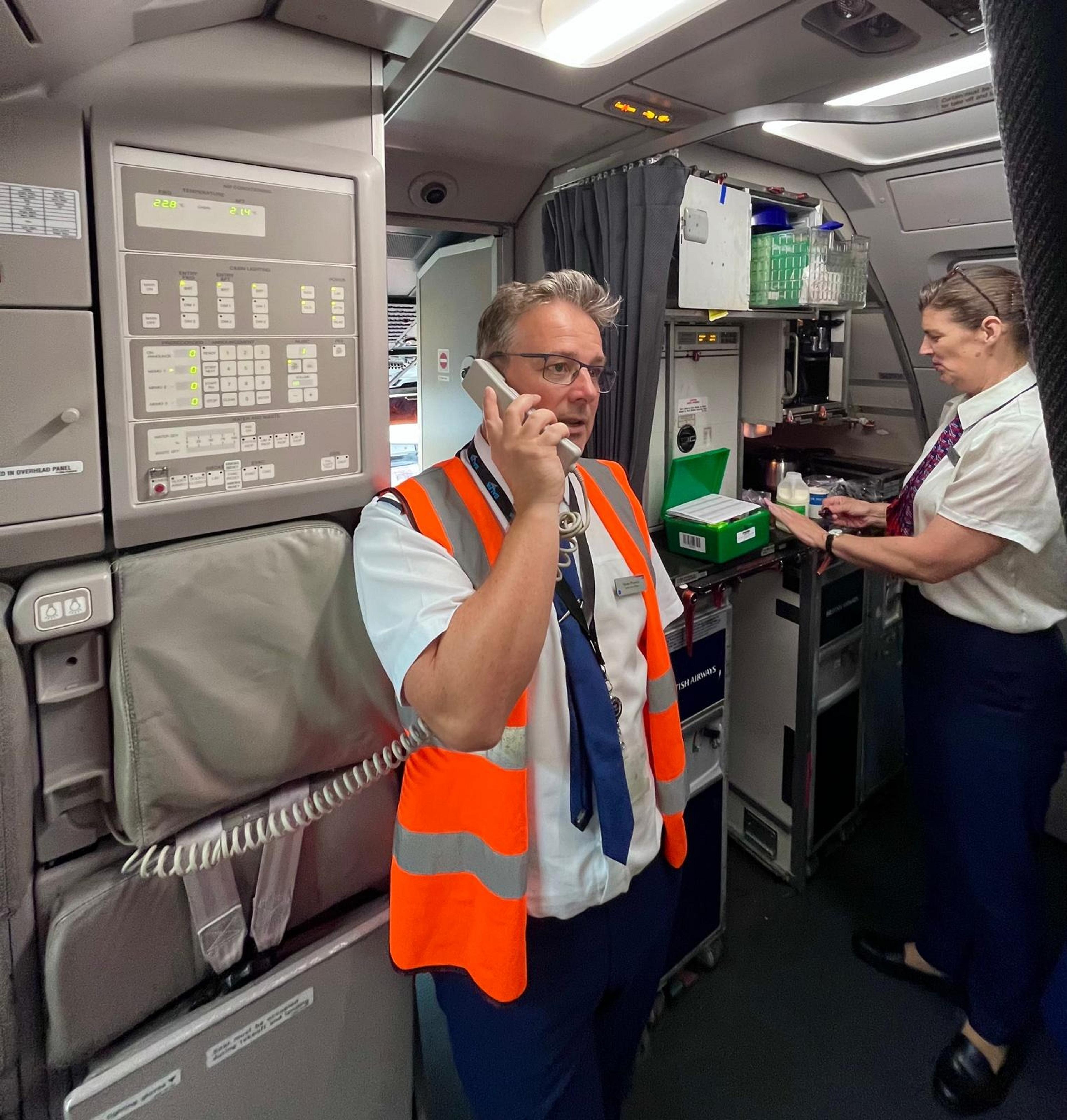 Inside a British Airways aircraft cabin, two crew members are engaged in their duties.