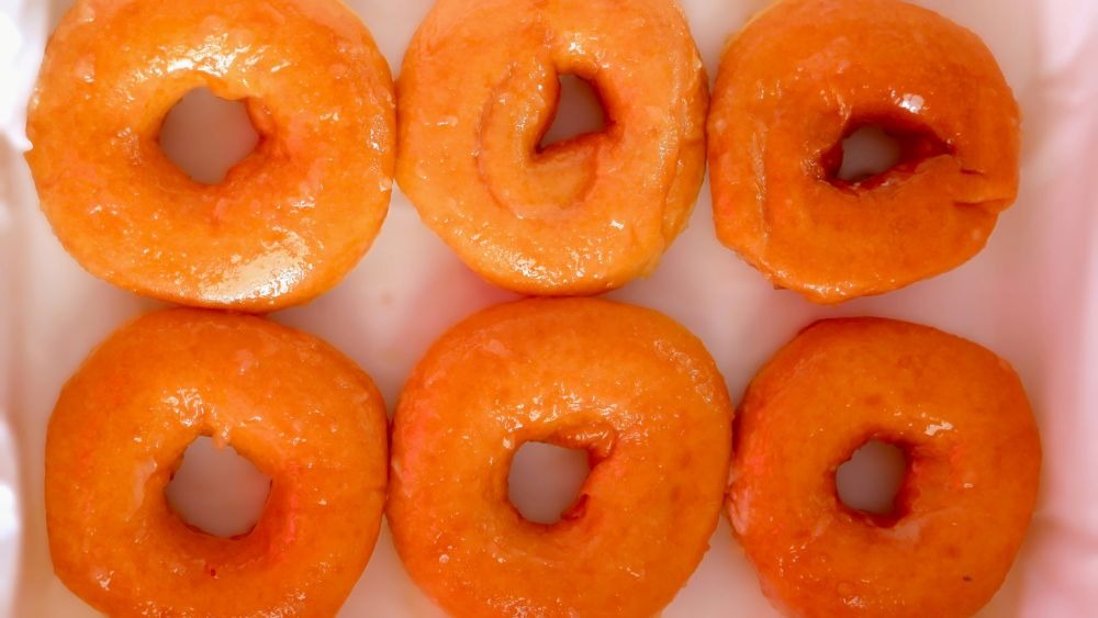 Half a dozen fresh, glossy donuts on a tray, likely from a bakery setting.