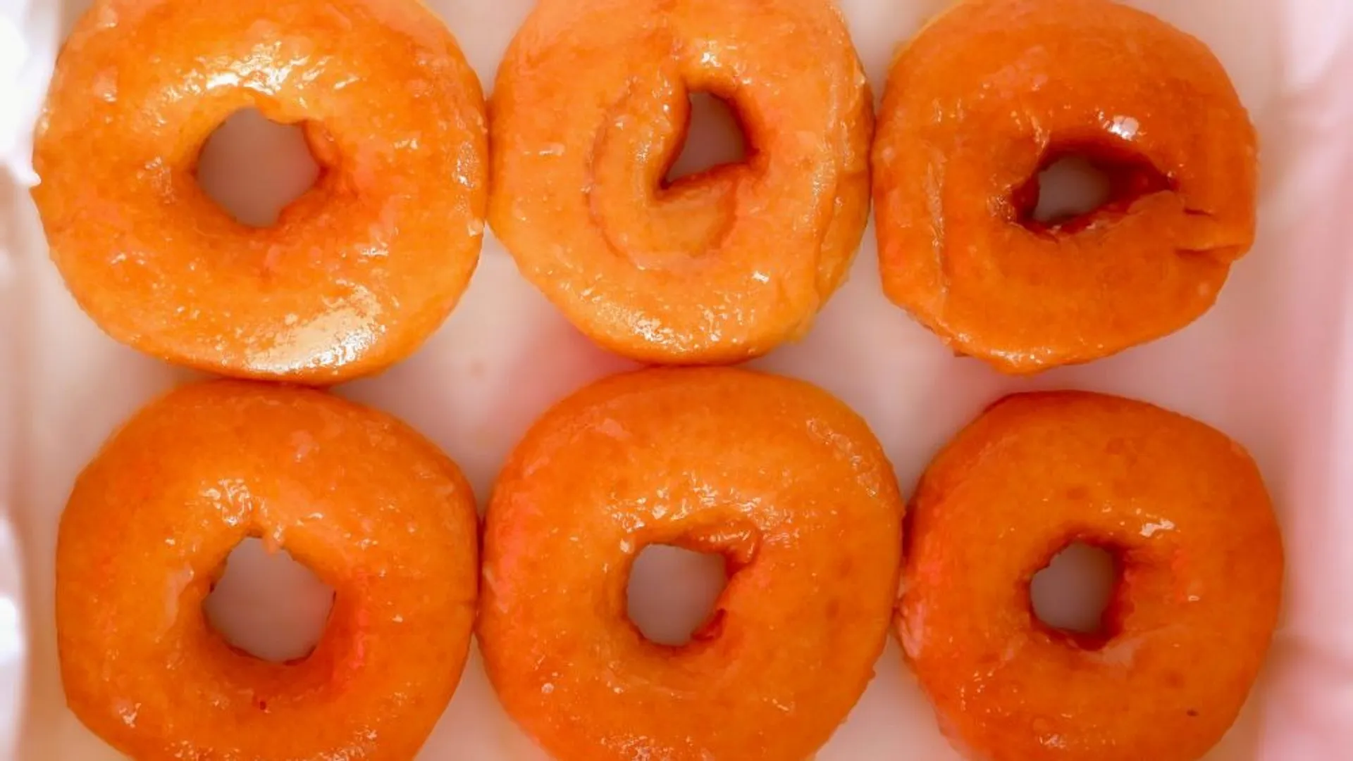Half a dozen fresh, glossy donuts on a tray, likely from a bakery setting.