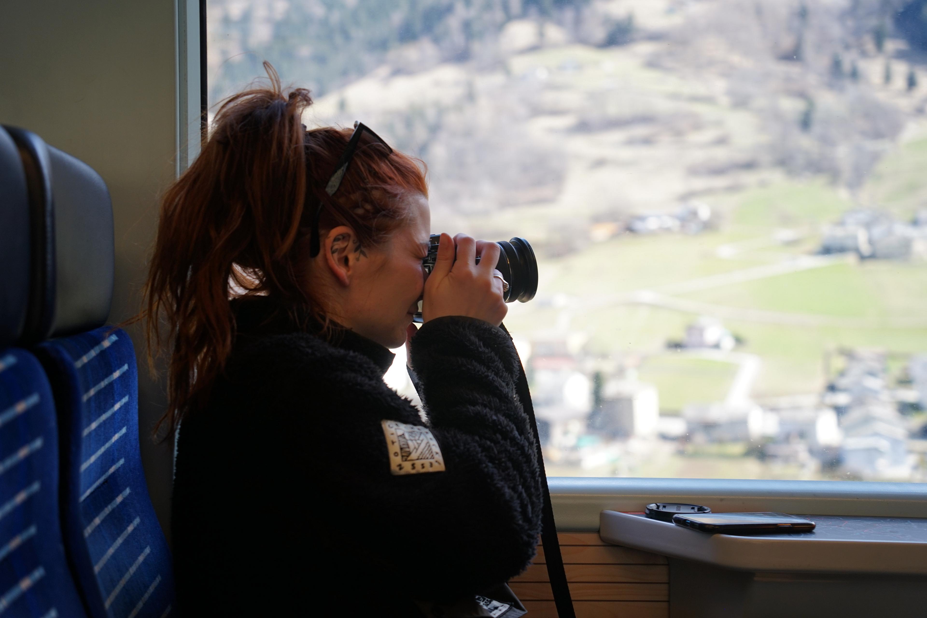 A person is taking photos of a scenic alpine landscape from a train window, possibly in Switzerland.