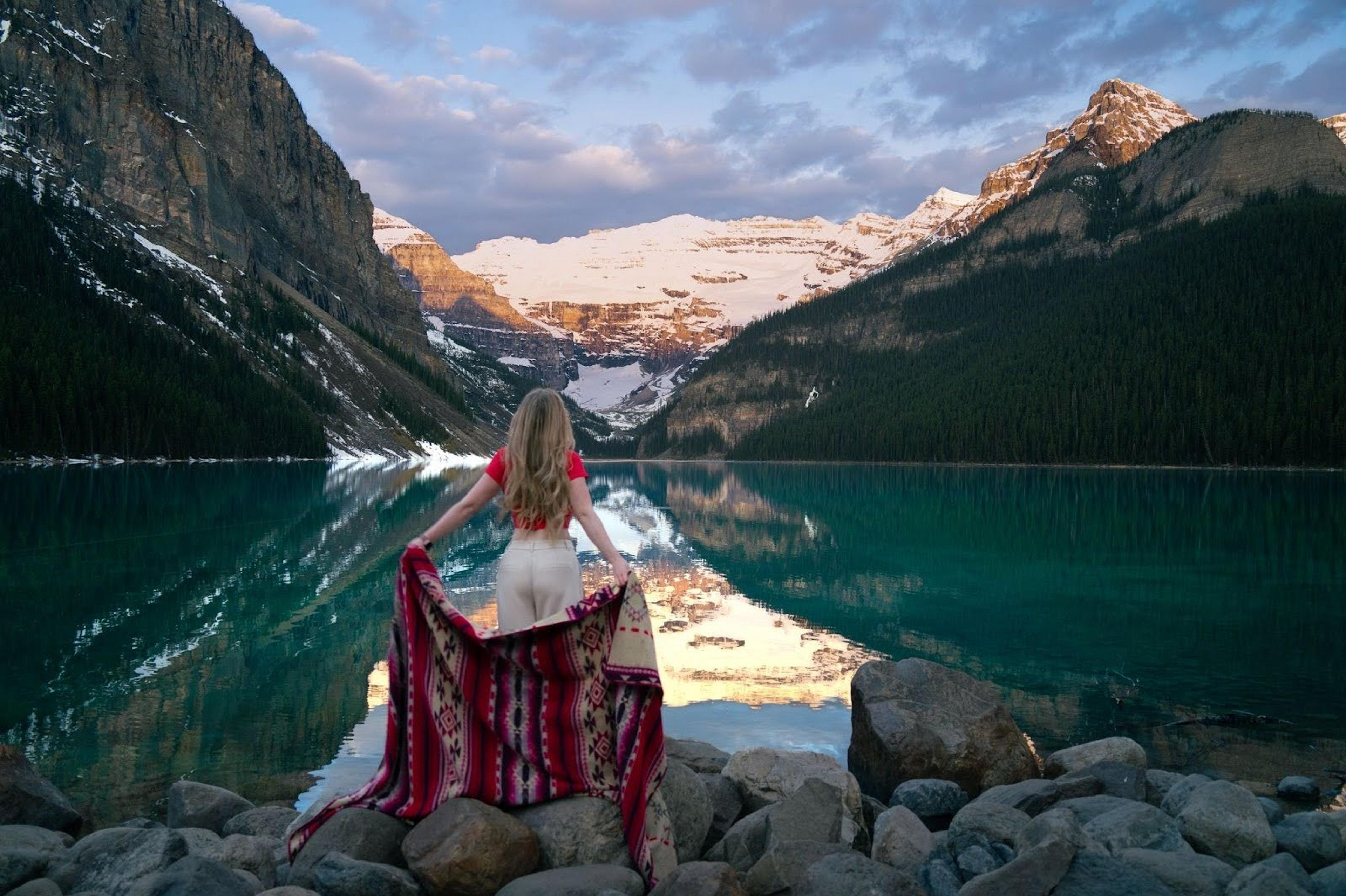 Kristi stands by the clear, reflective waters of Lake Louise, surrounded by the Canadian Rockies.