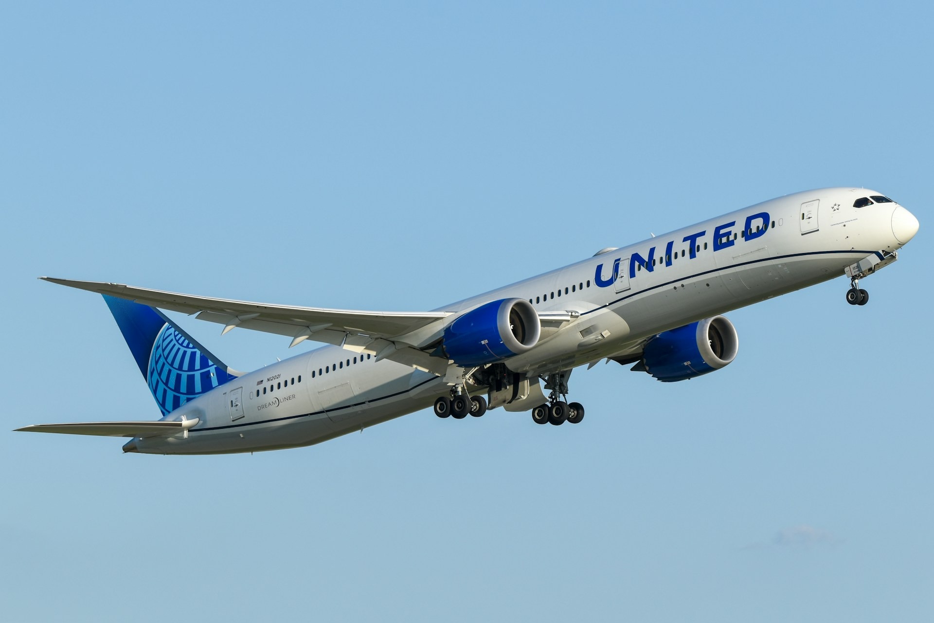 A United Airlines Boeing 787 Dreamliner soars into a clear blue sky.