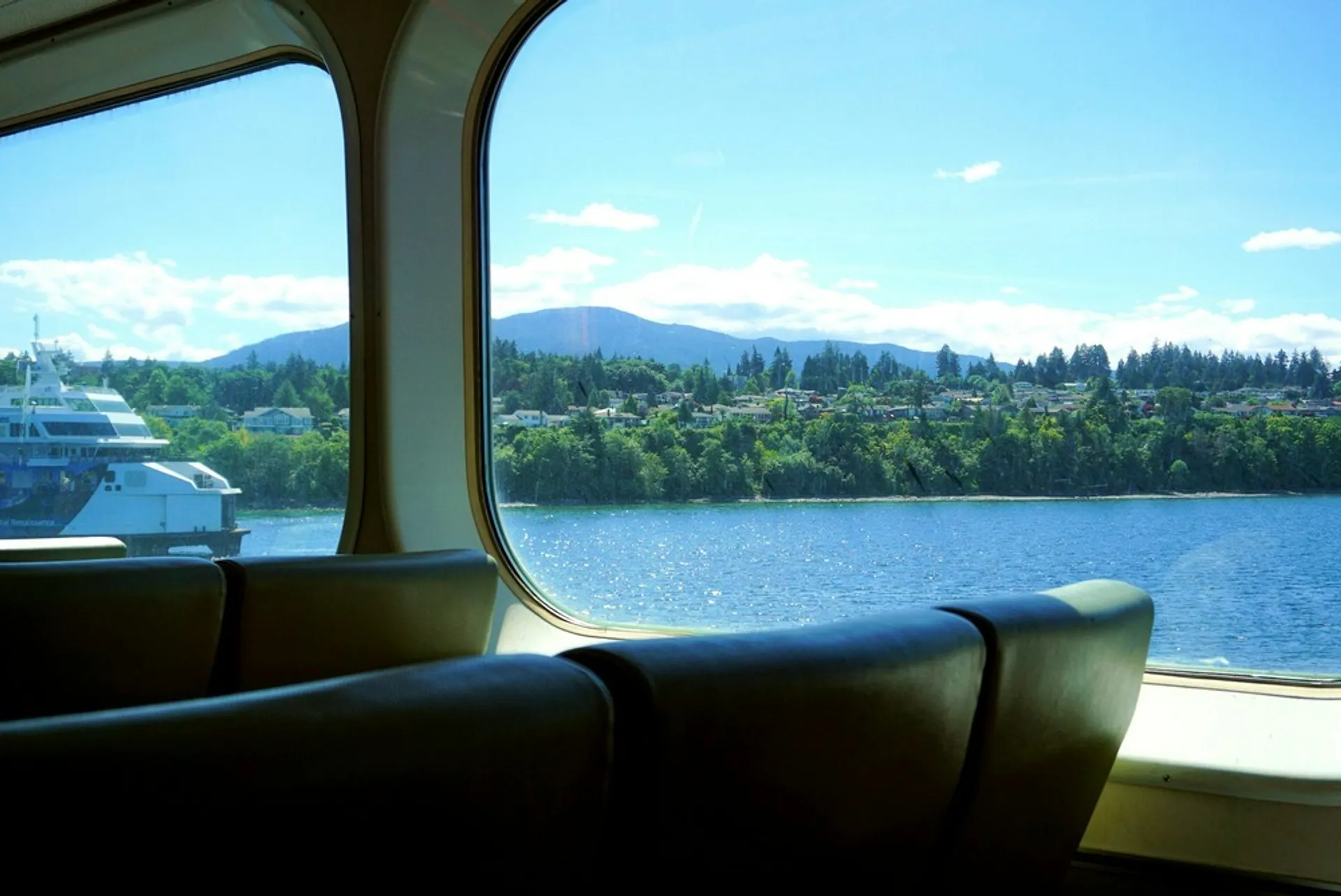 A view from the inside of a ferry on the Swartz Bay to Tsawwassen route, capturing the lush coastline and distant mountains under a clear blue sky.