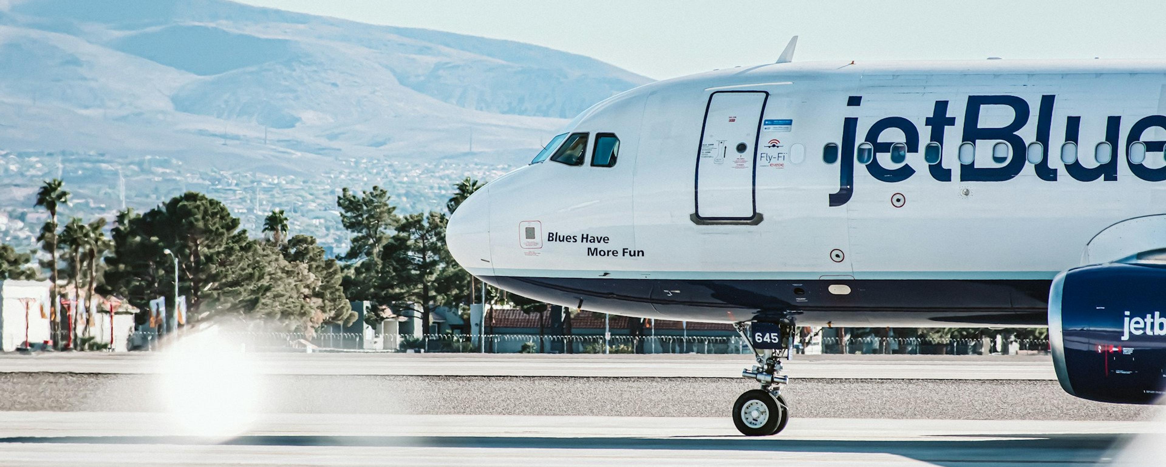 A JetBlue airplane taxis on a runway with the mountainous landscape of Las Vegas in the background.