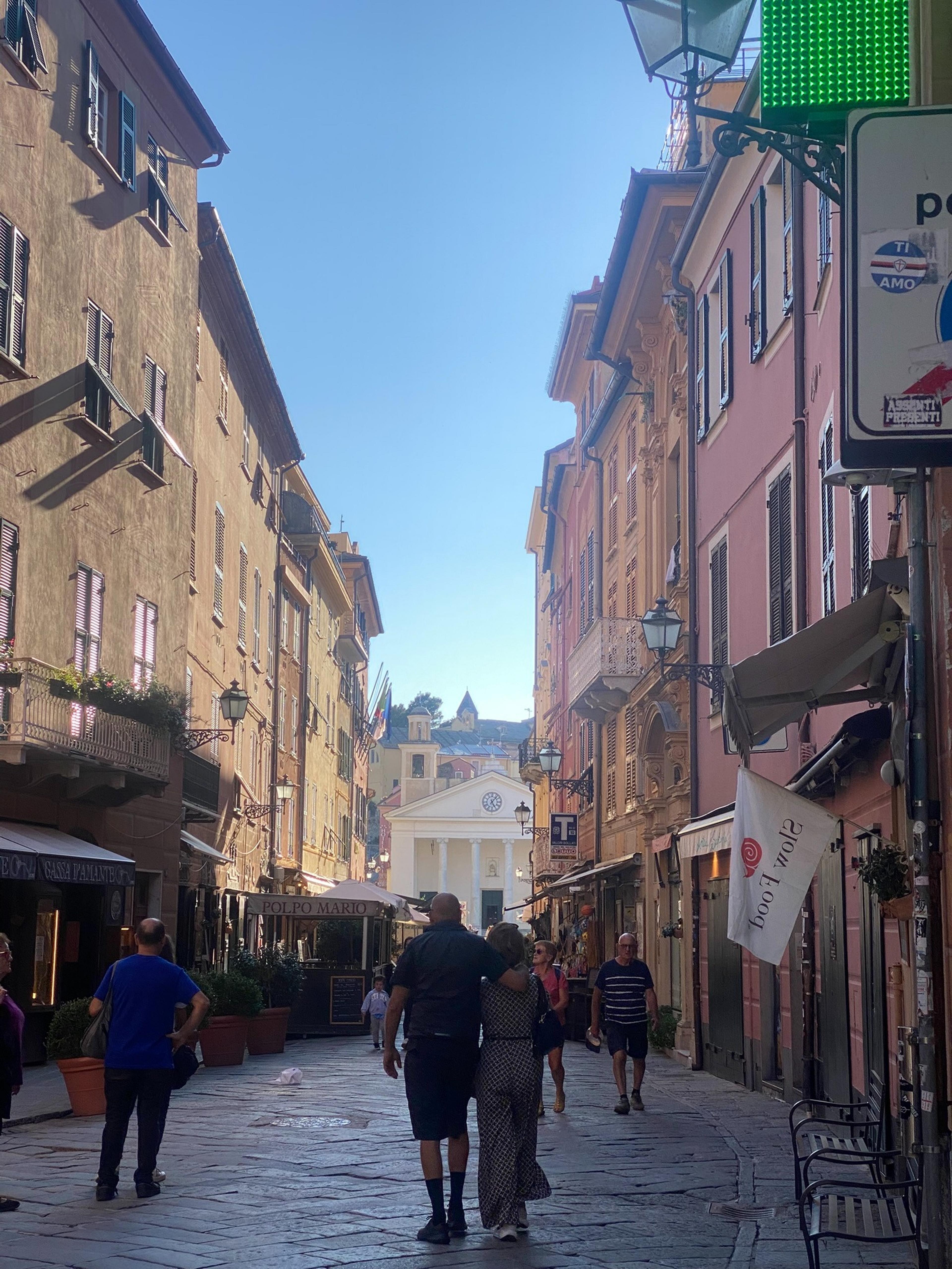 A picturesque street in Sestri Levante Italy, features charming buildings with balconies and people strolling along the cobblestone path.